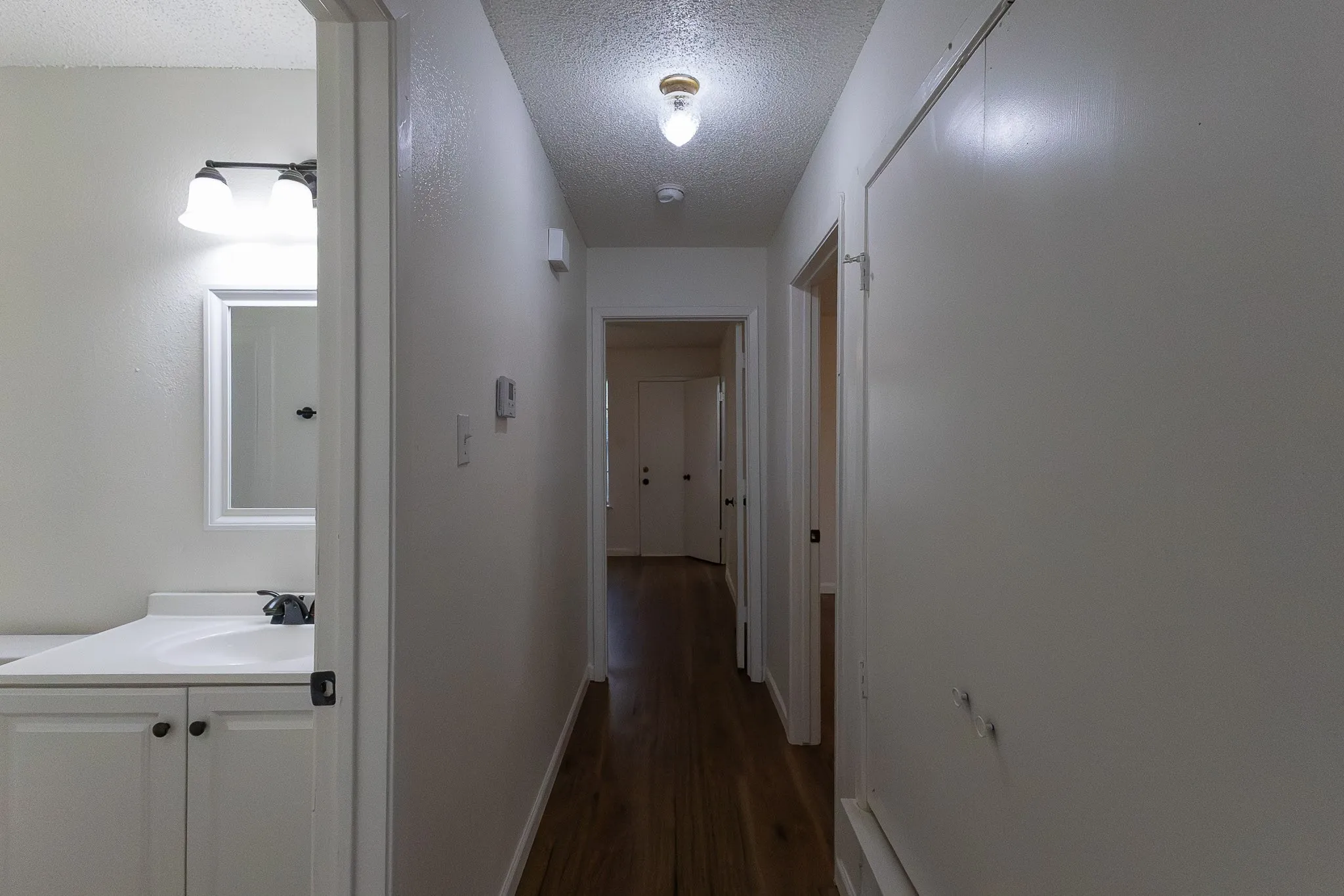 White vanity with a single basin sink, wall-mounted light fixture, and wood-finish flooring
