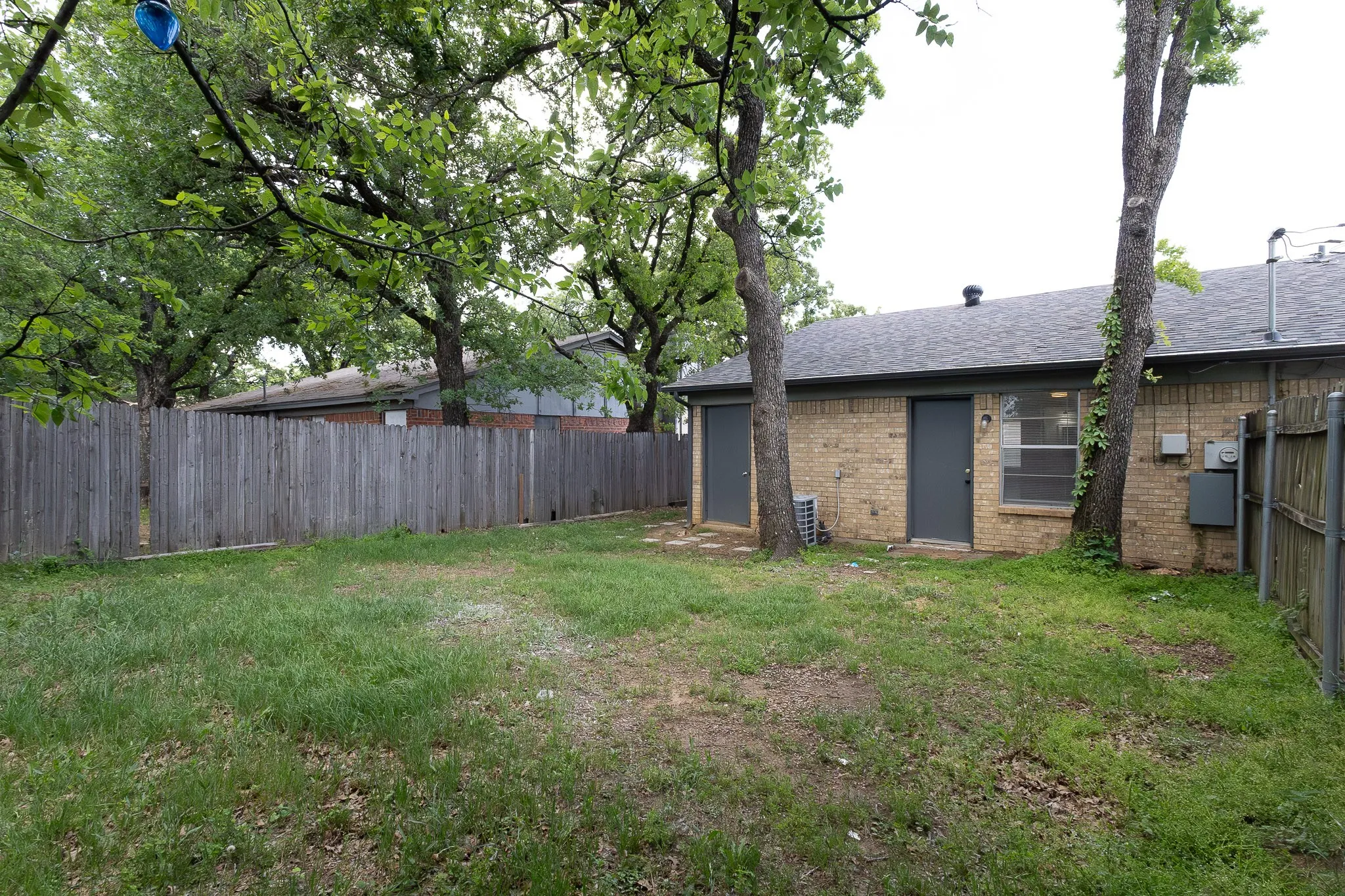 Expansive fenced yard with mature trees, brick exterior, and multiple exterior access doors