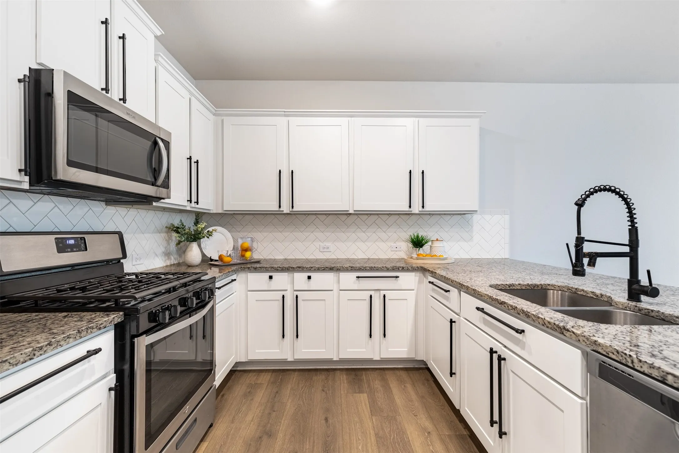 U-shaped kitchen featuring white cabinetry, stainless steel appliances, a tile backsplash, light-toned countertops, and wood-finish flooring
