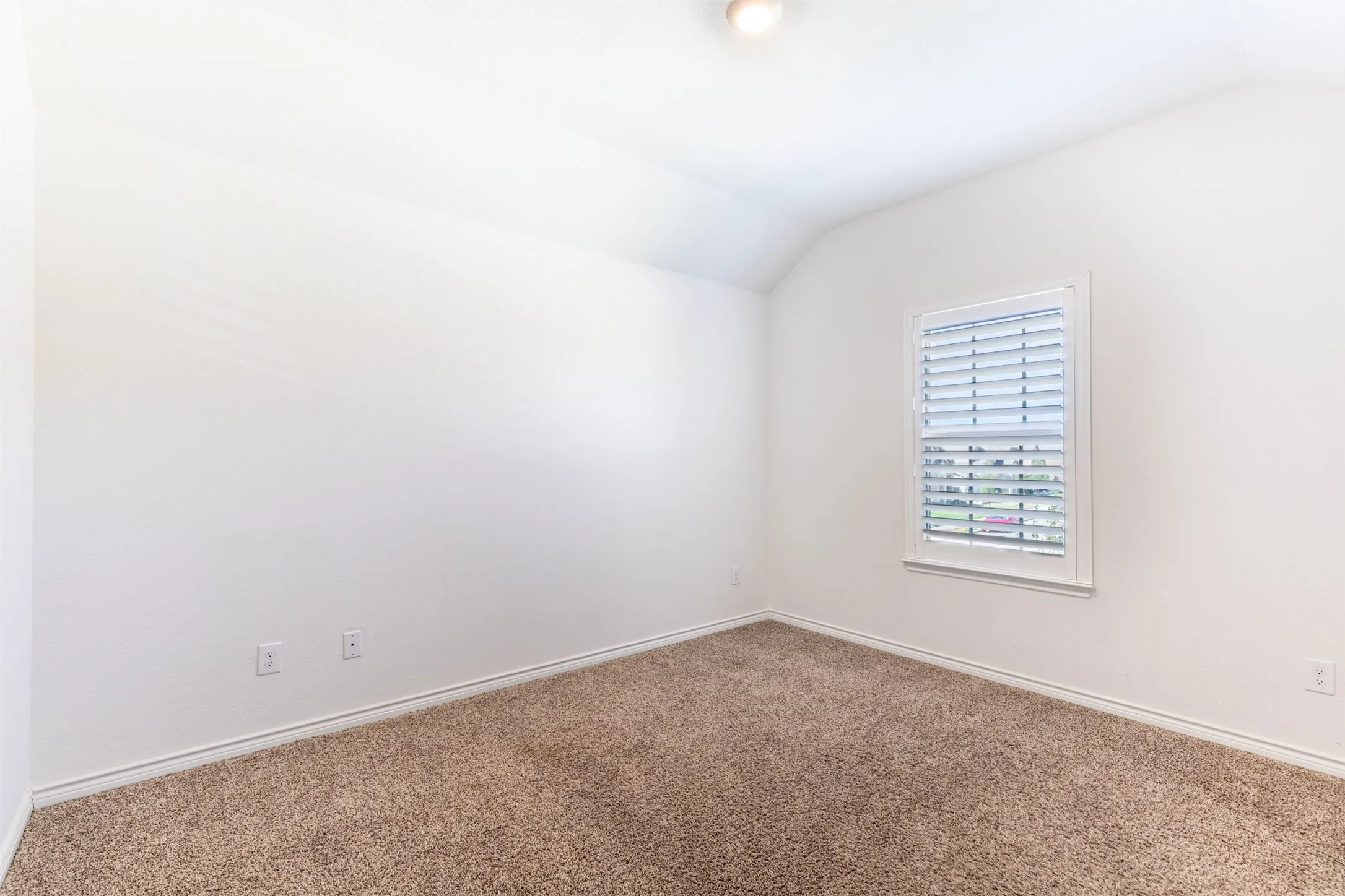 Vaulted ceiling with a flush-mount light fixture, a single window with white plantation shutters, and light brown carpeting
