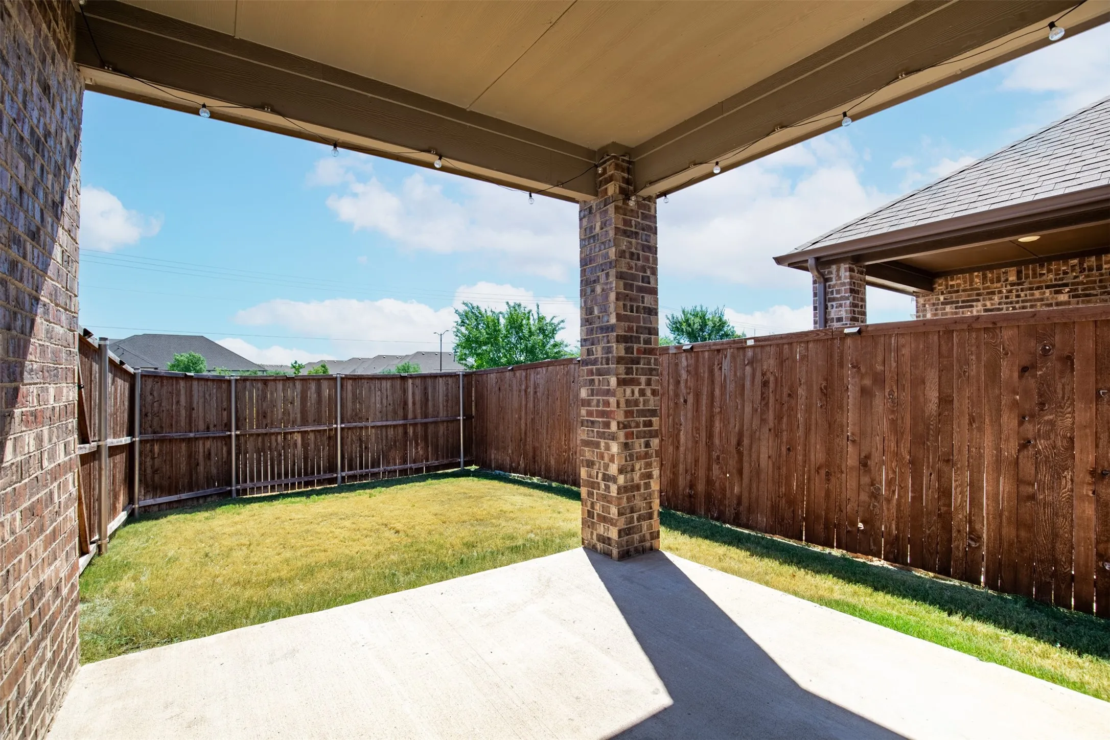 Covered patio featuring concrete flooring and string lighting, enclosed by a wood privacy fence