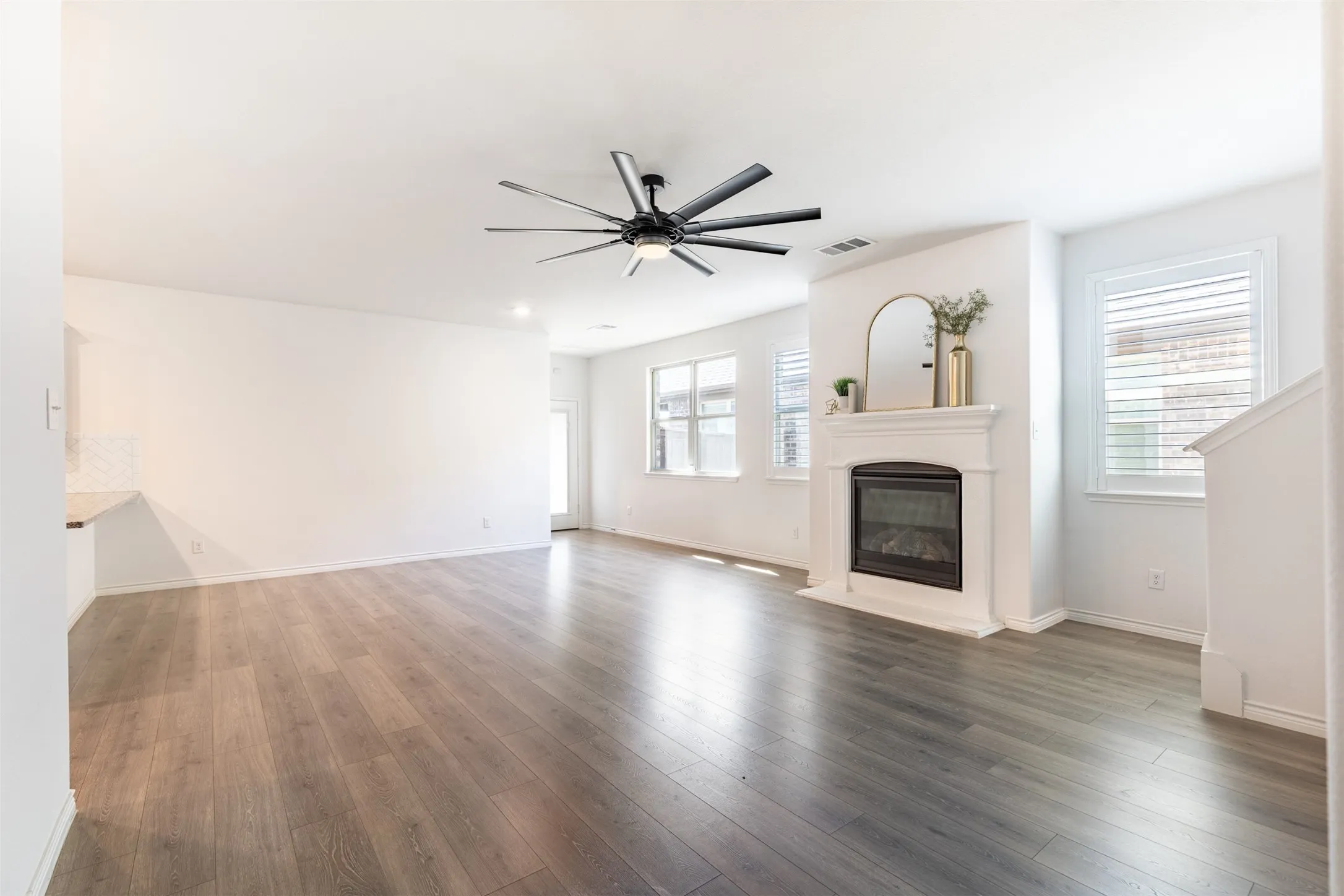Wood-finish flooring throughout, white walls, built-in fireplace with a white mantel, and a black ceiling fan