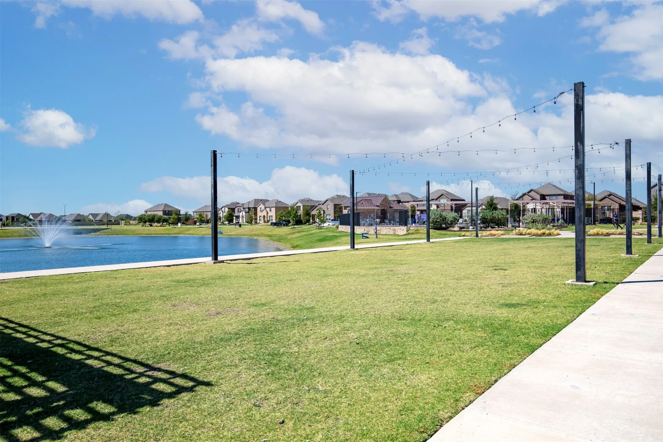 Expansive green space with a concrete pathway and string lighting
