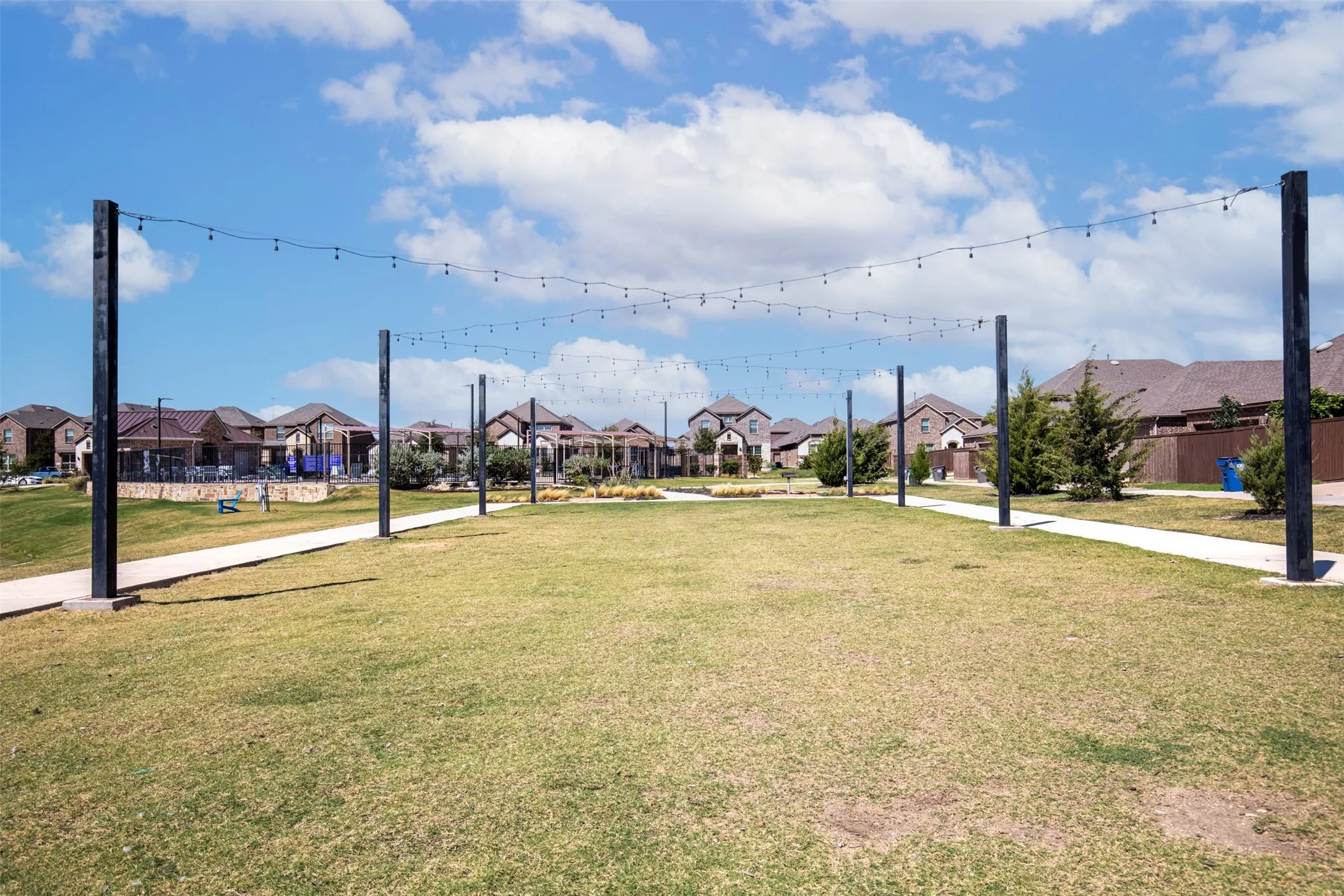 Expansive green space featuring string lighting, paved walking paths, and surrounding residential structures