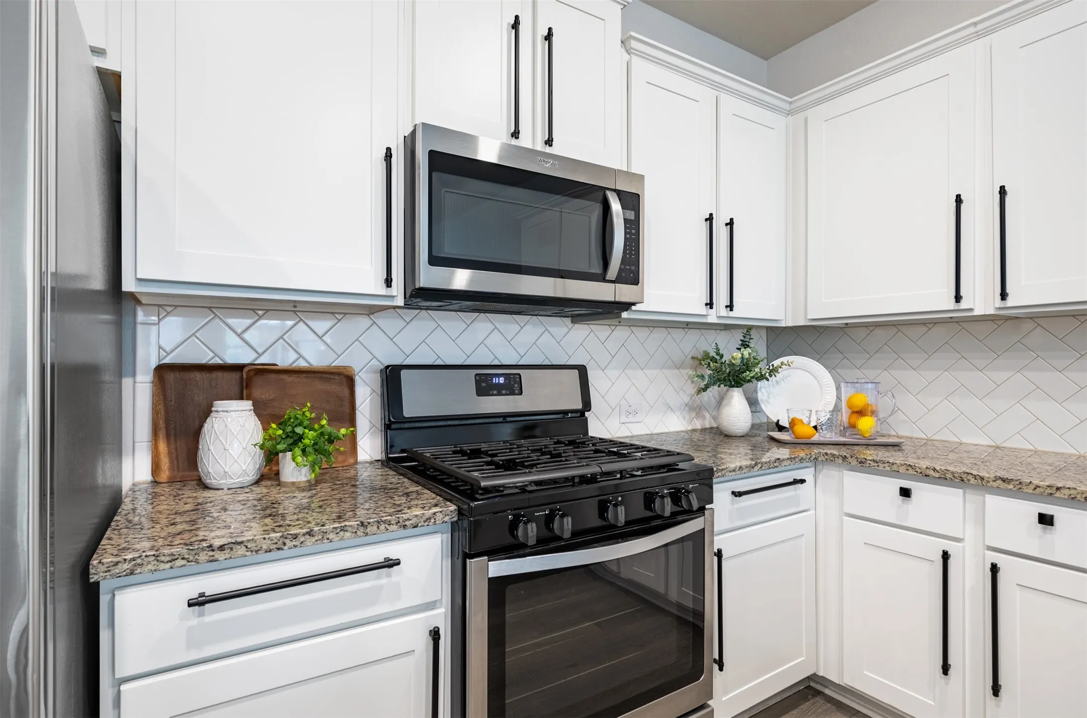 White cabinetry with dark hardware, stainless steel appliances, herringbone tile backsplash, and speckled countertops