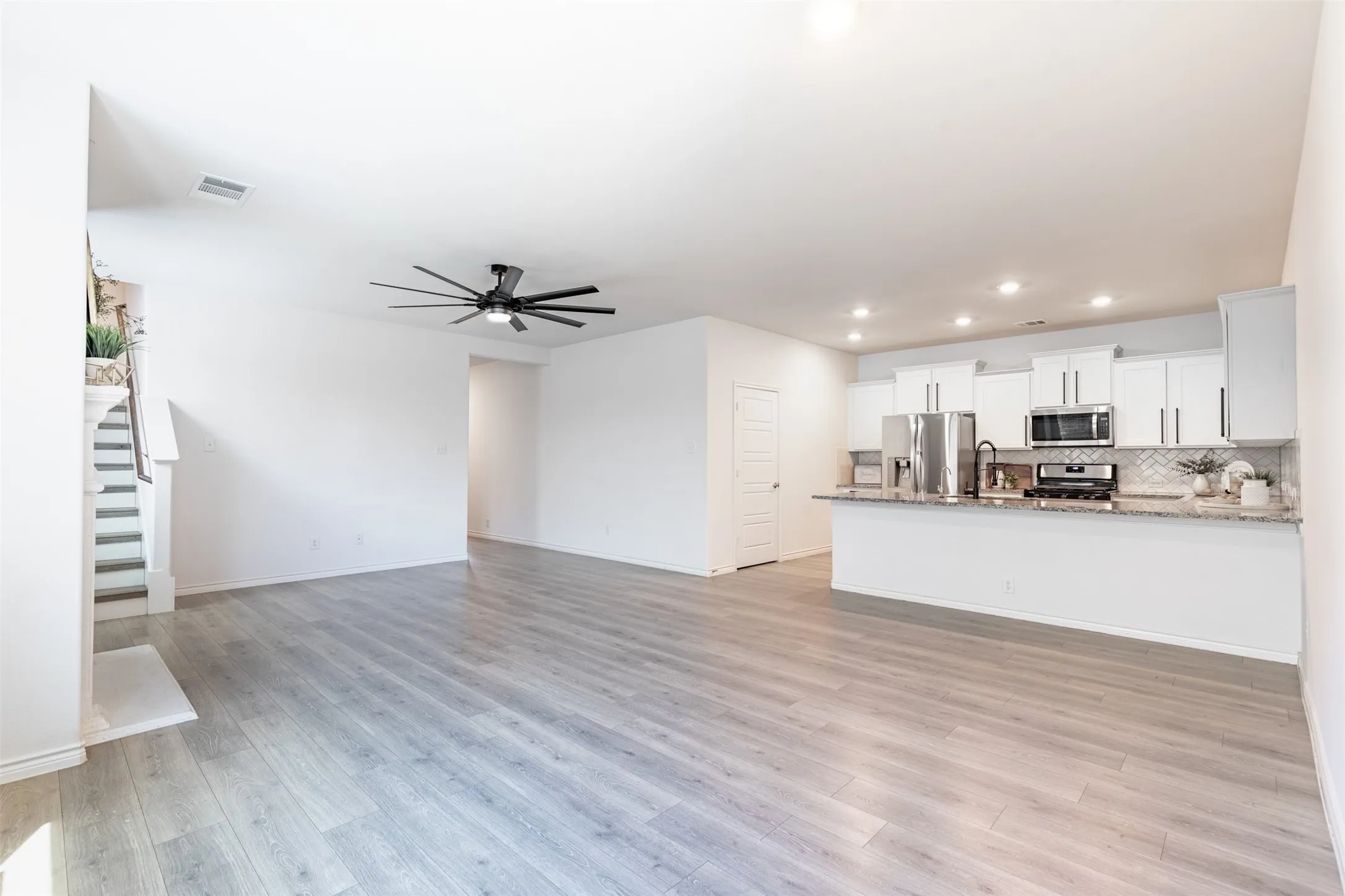 Open concept living space with wood-finish flooring, a modern ceiling fan, and a kitchen featuring white cabinetry, stainless steel appliances, and an island with a stone countertop