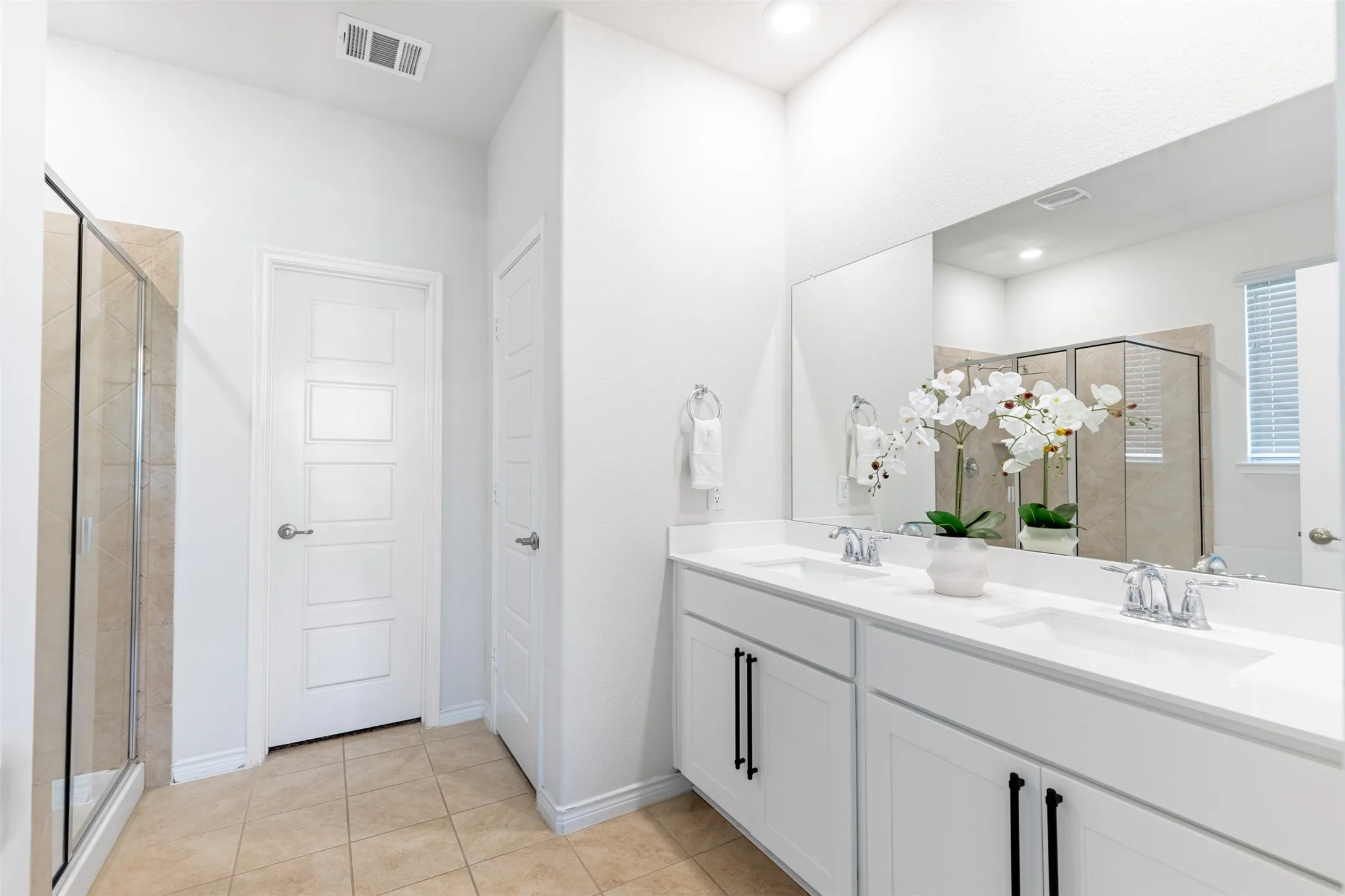 Dual vanity with undermount sinks and chrome fixtures, white cabinetry with matte black hardware, and a glass-enclosed shower with tiled walls