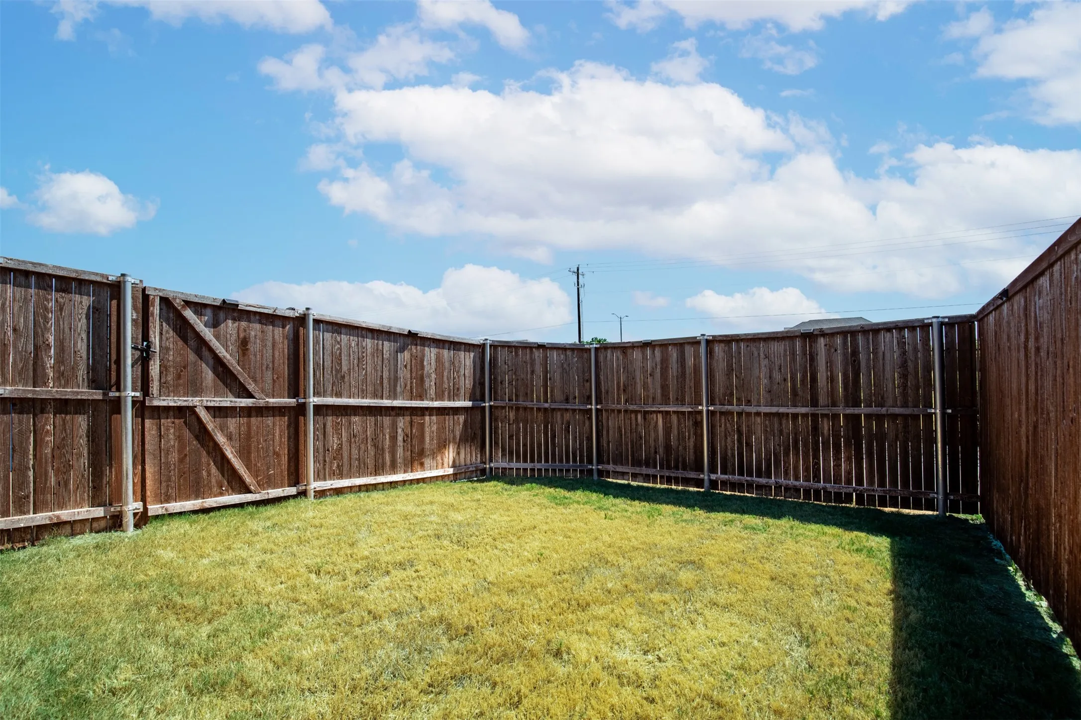 Expansive backyard featuring a manicured lawn, wood privacy fencing, and a wood gate