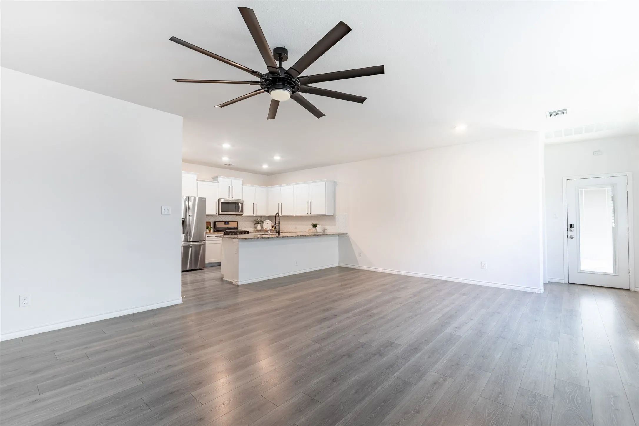 Open-concept living space featuring wood-finish flooring, a contemporary ceiling fan, recessed lighting, and a kitchen with white cabinetry and stainless steel appliances