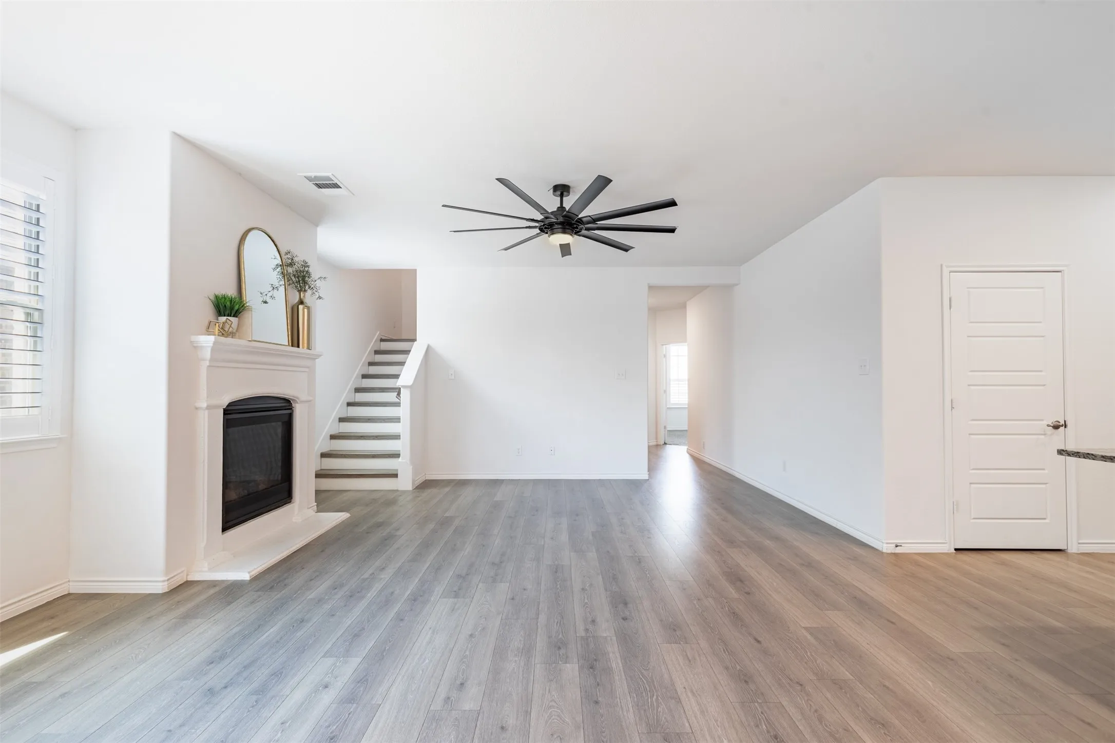 Living area featuring wood-finish flooring, a fireplace with a detailed mantel, a ceiling fan, and a paneled door