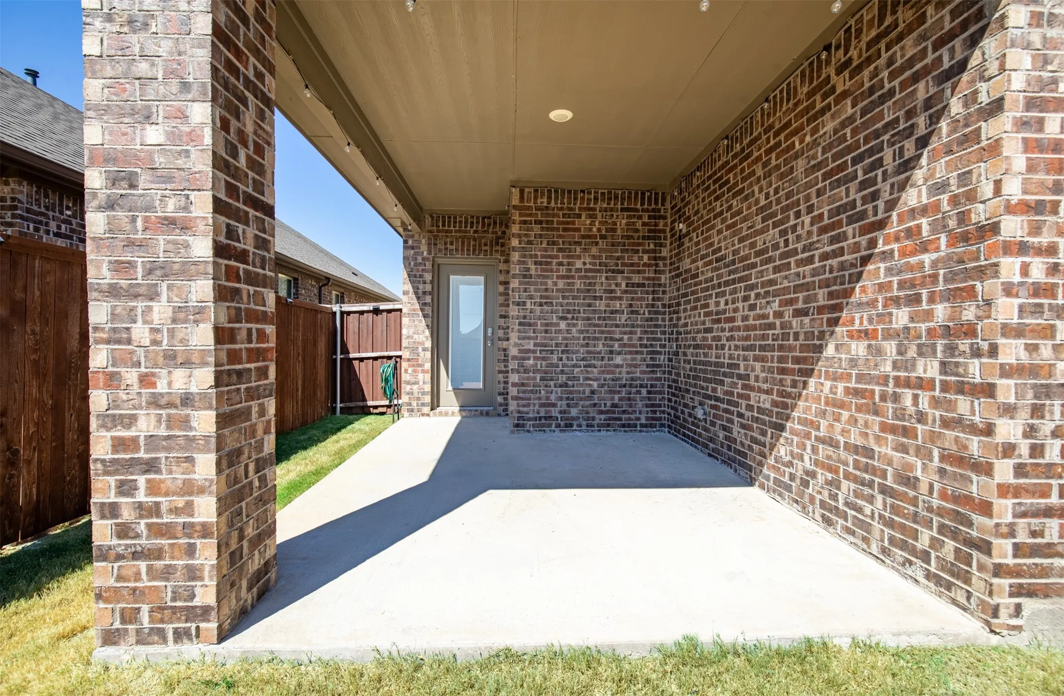 Covered patio featuring brick columns, a concrete surface, and a recessed light fixture