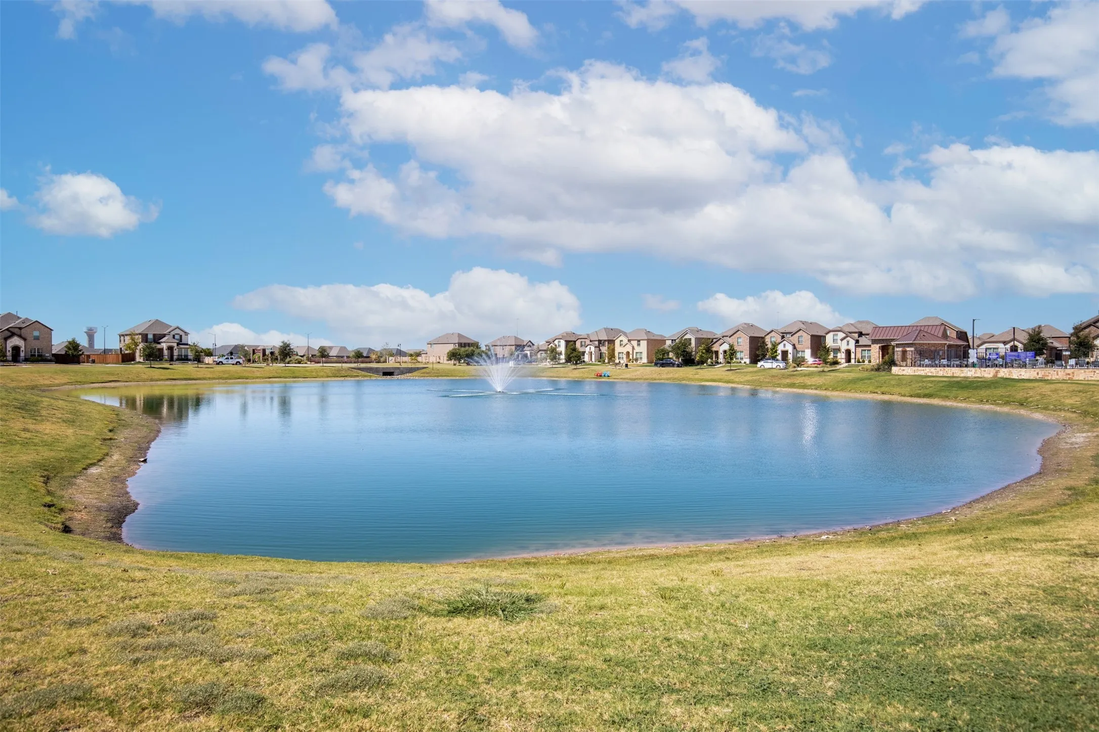 Expansive lake with a central fountain, surrounded by manicured grassy areas and residential properties