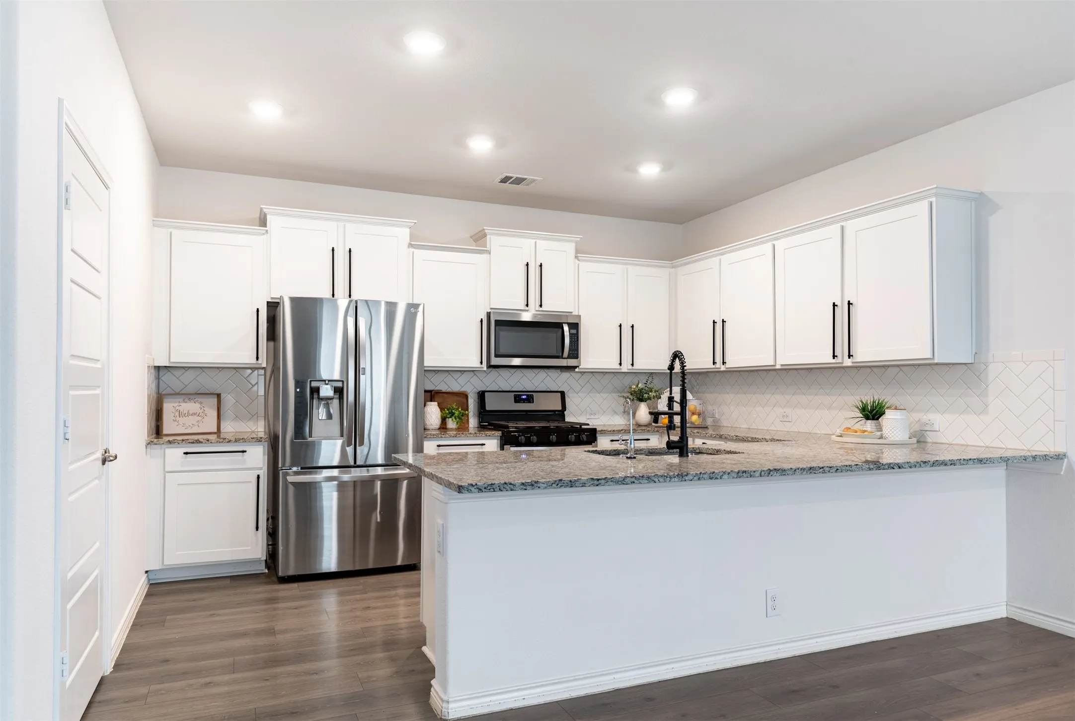White cabinetry, stainless steel appliances, granite countertops, tile backsplash, and wood-finish flooring