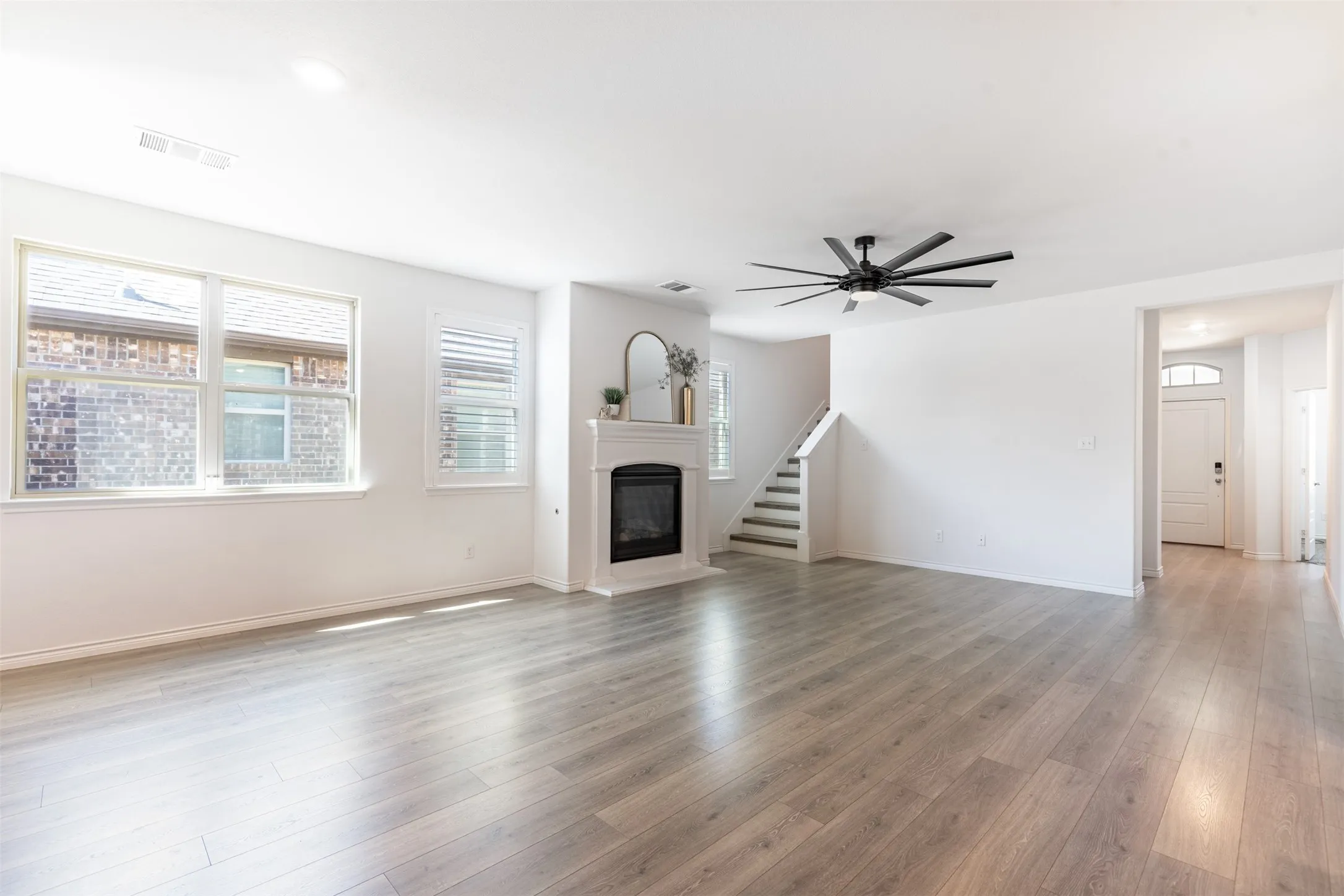 Spacious living area featuring light wood-finish flooring, a white mantel fireplace, and a contemporary ceiling fan