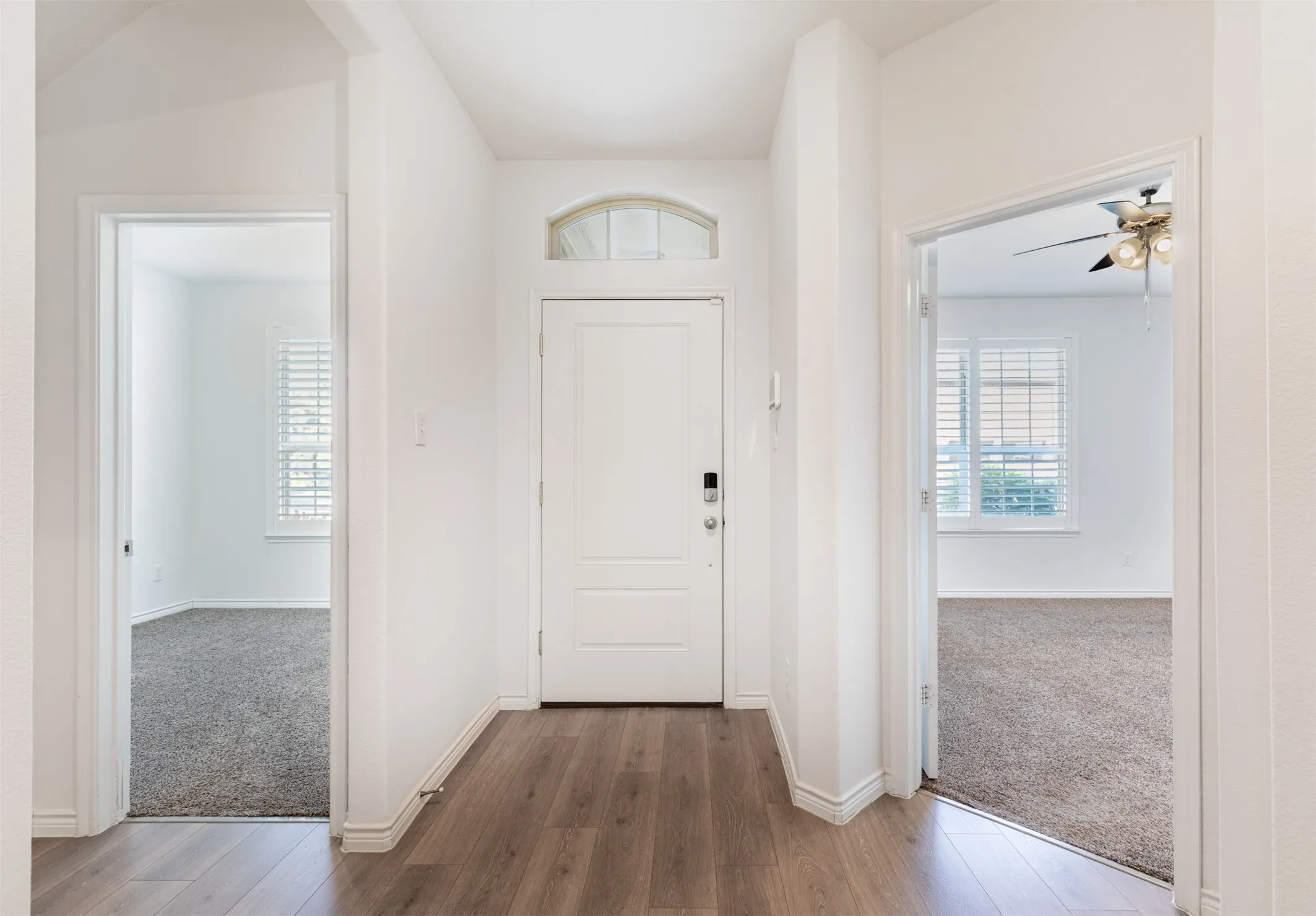 Entryway featuring wood-finish flooring, a white paneled door with an arched transom, and white trim