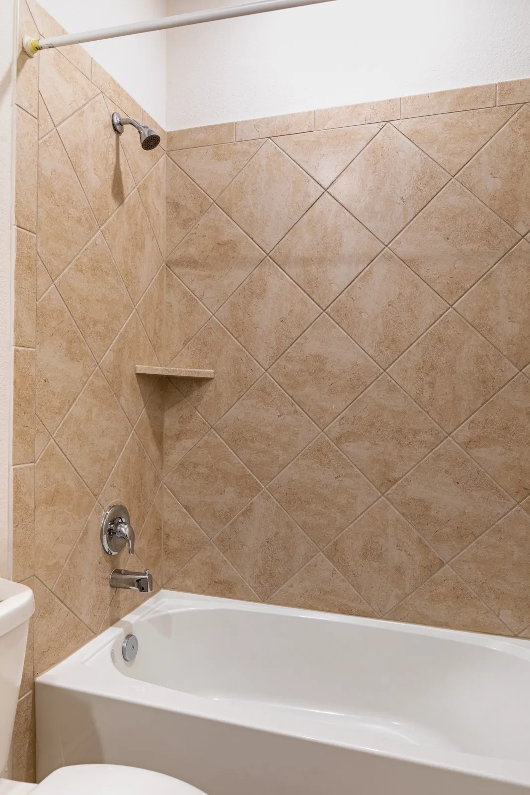 Bathtub with a shower fixture, chrome plumbing, and diagonal-set wall tiling