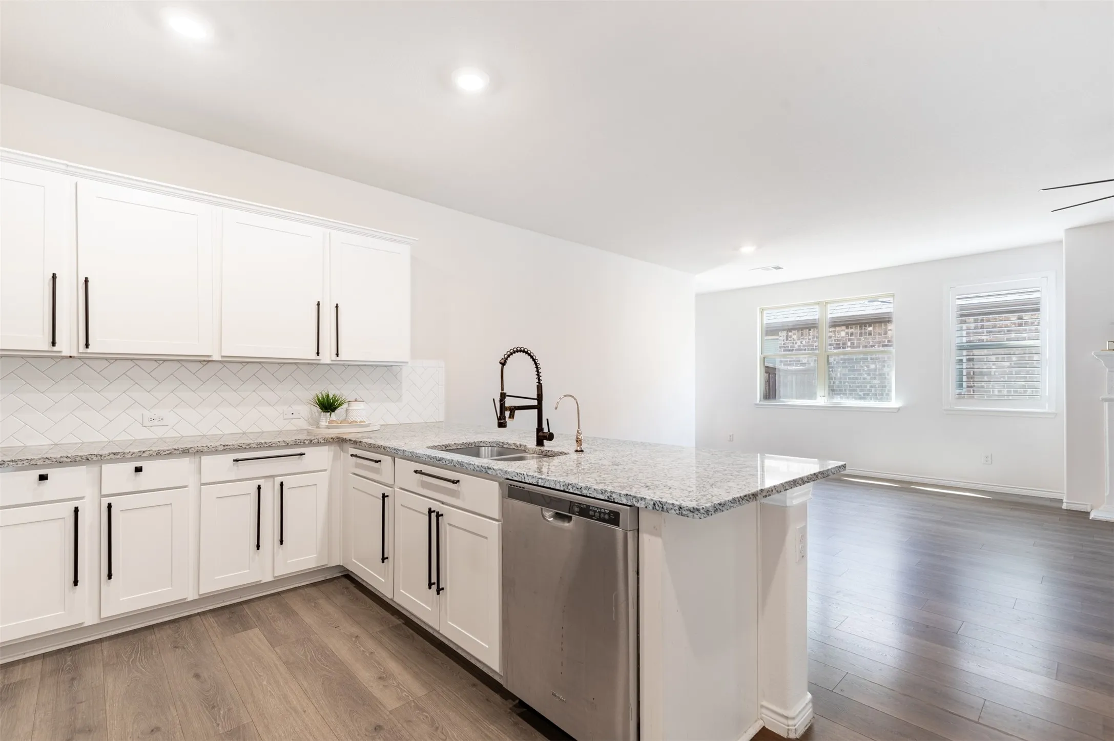 Kitchen island with granite countertop, stainless steel appliances, white cabinetry, and wood-finish flooring