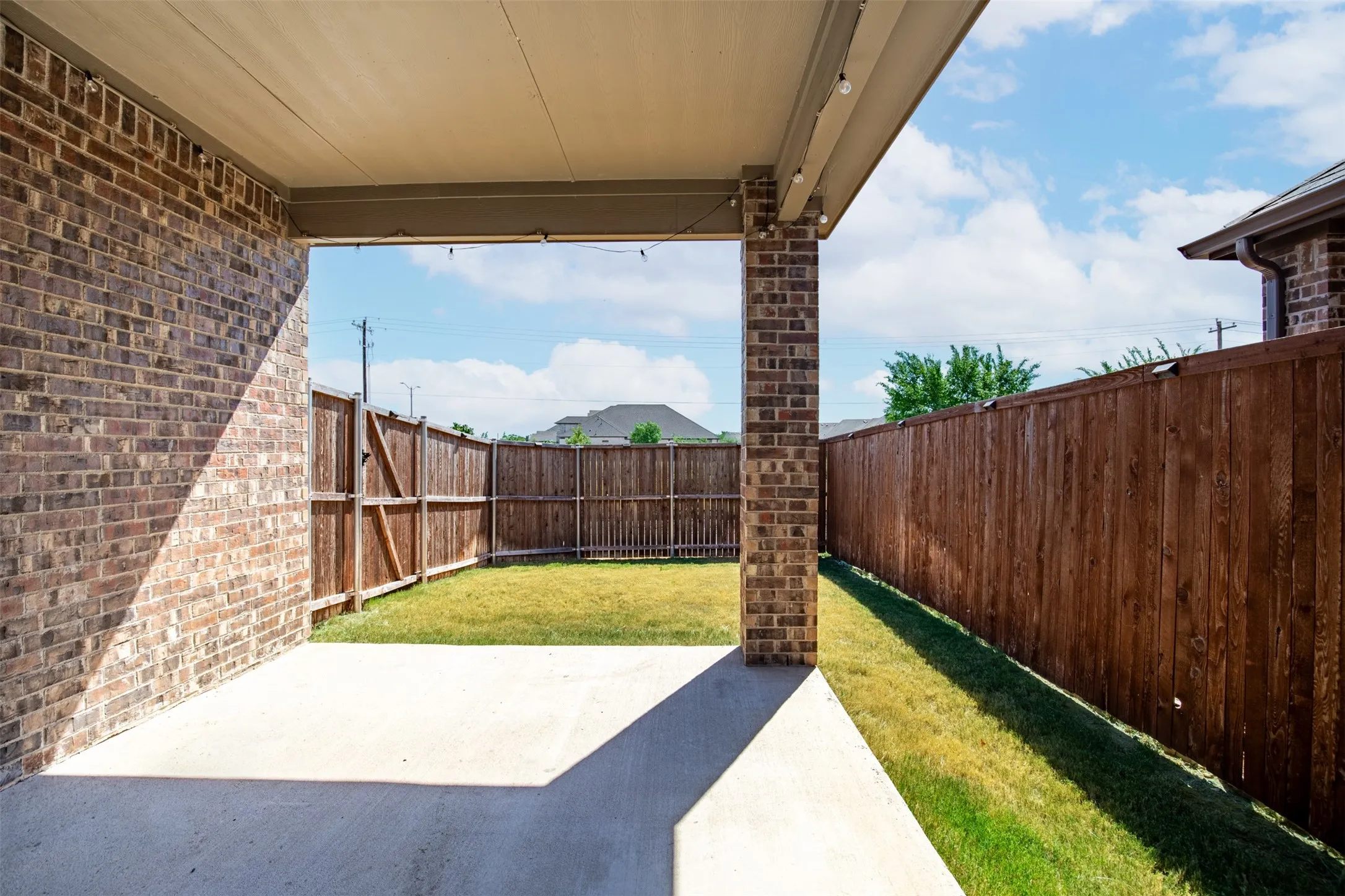 Covered patio featuring brick columns, a concrete floor, and a wood privacy fence