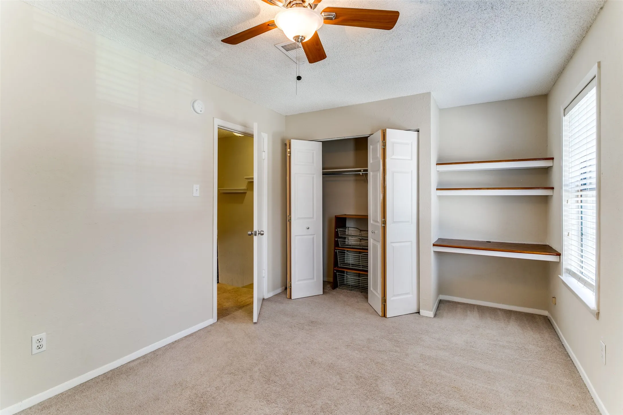 Carpeted room featuring a ceiling fan, a bi-fold closet, and built-in shelving with a desk surface