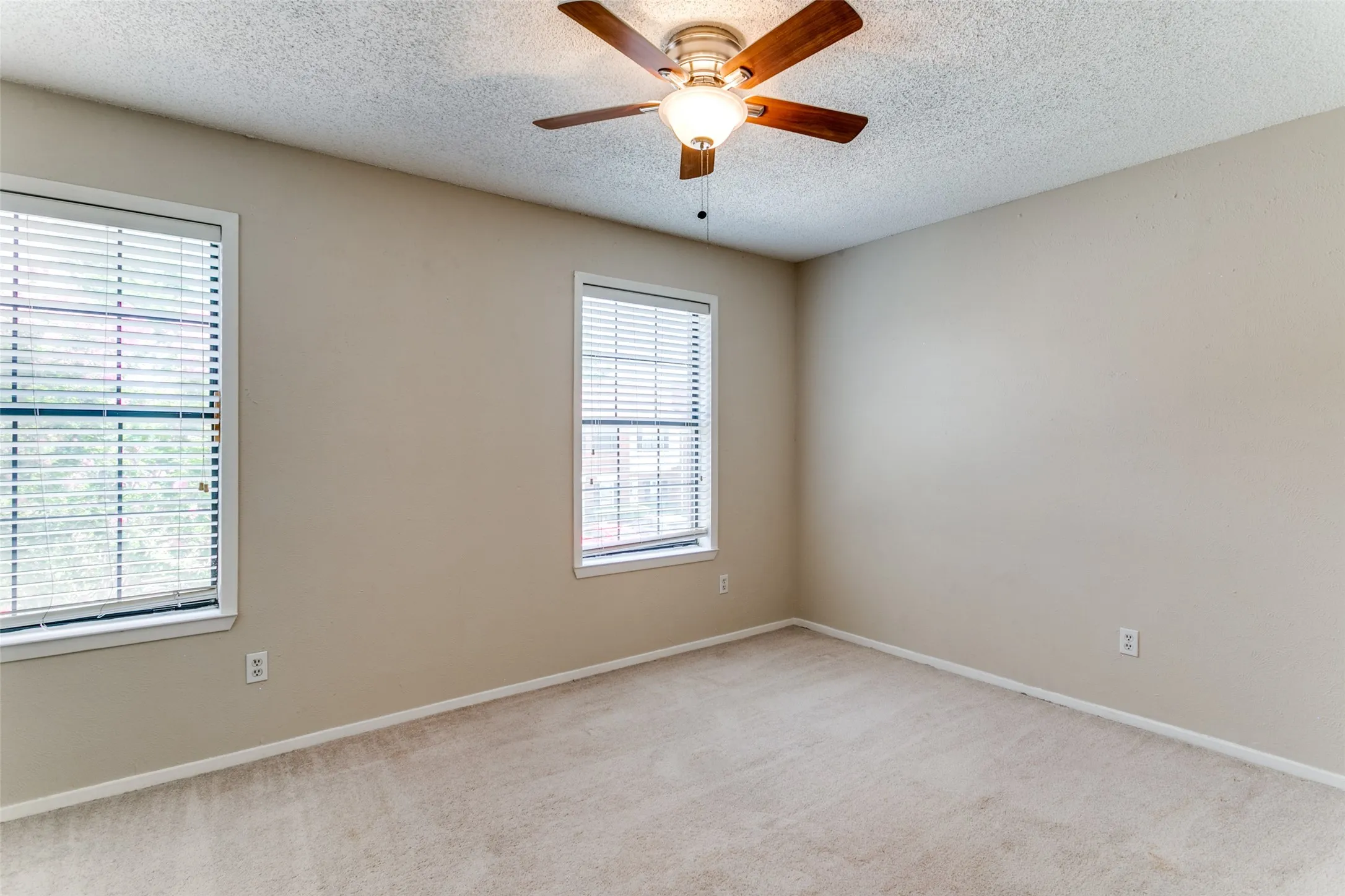 Neutral wall tones, two windows with blinds, and a ceiling fan with integrated lighting