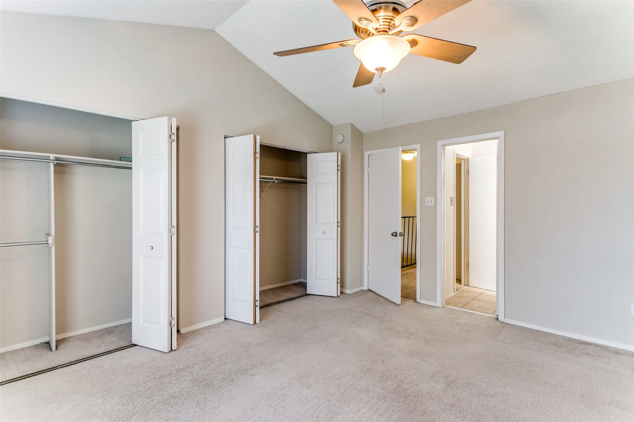 Vaulted ceiling, ceiling fan with integrated lighting, two bi-fold door closets, neutral wall paint, and carpet flooring