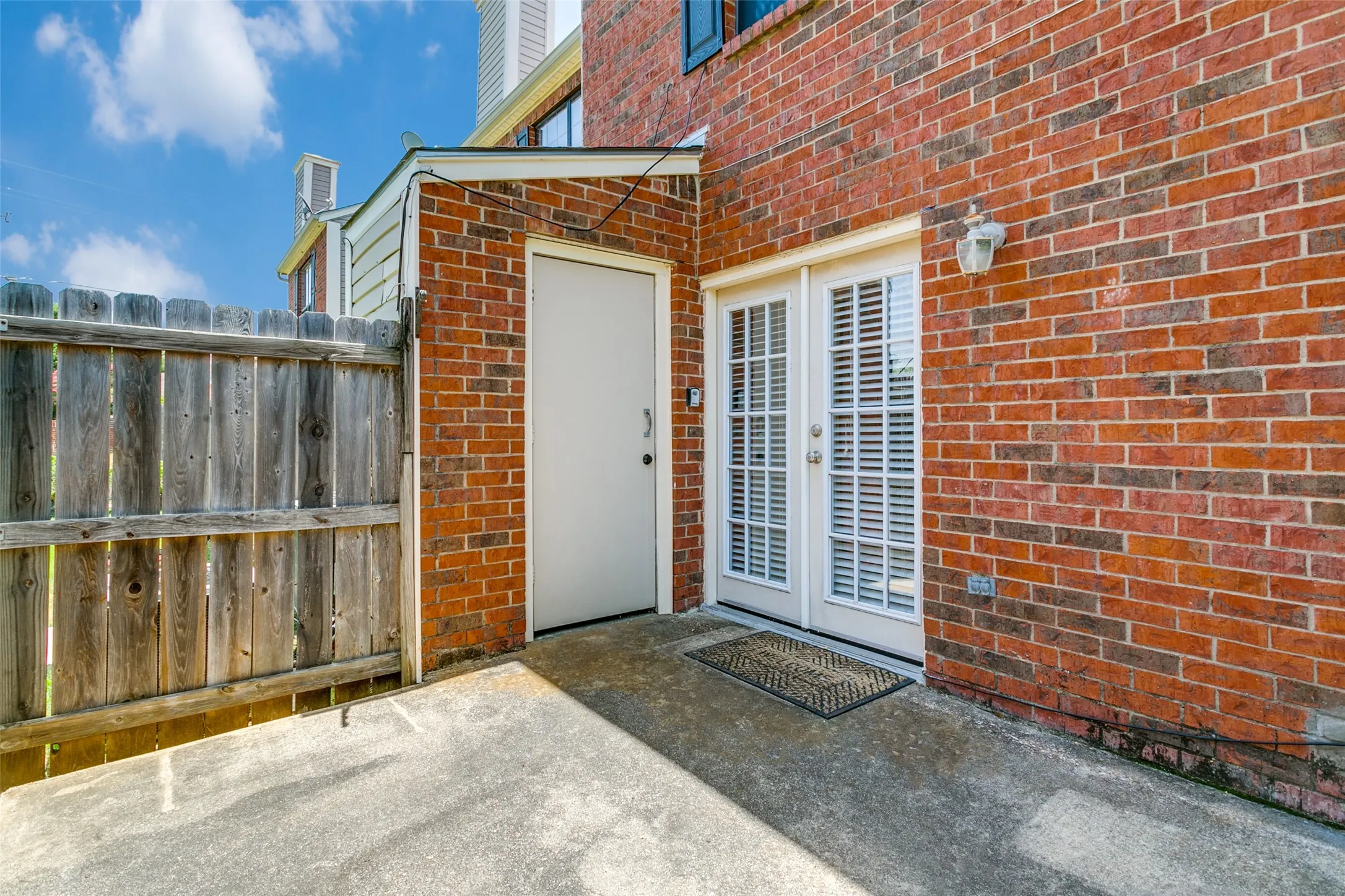 Brick exterior with a privacy fence, concrete patio, and white French doors