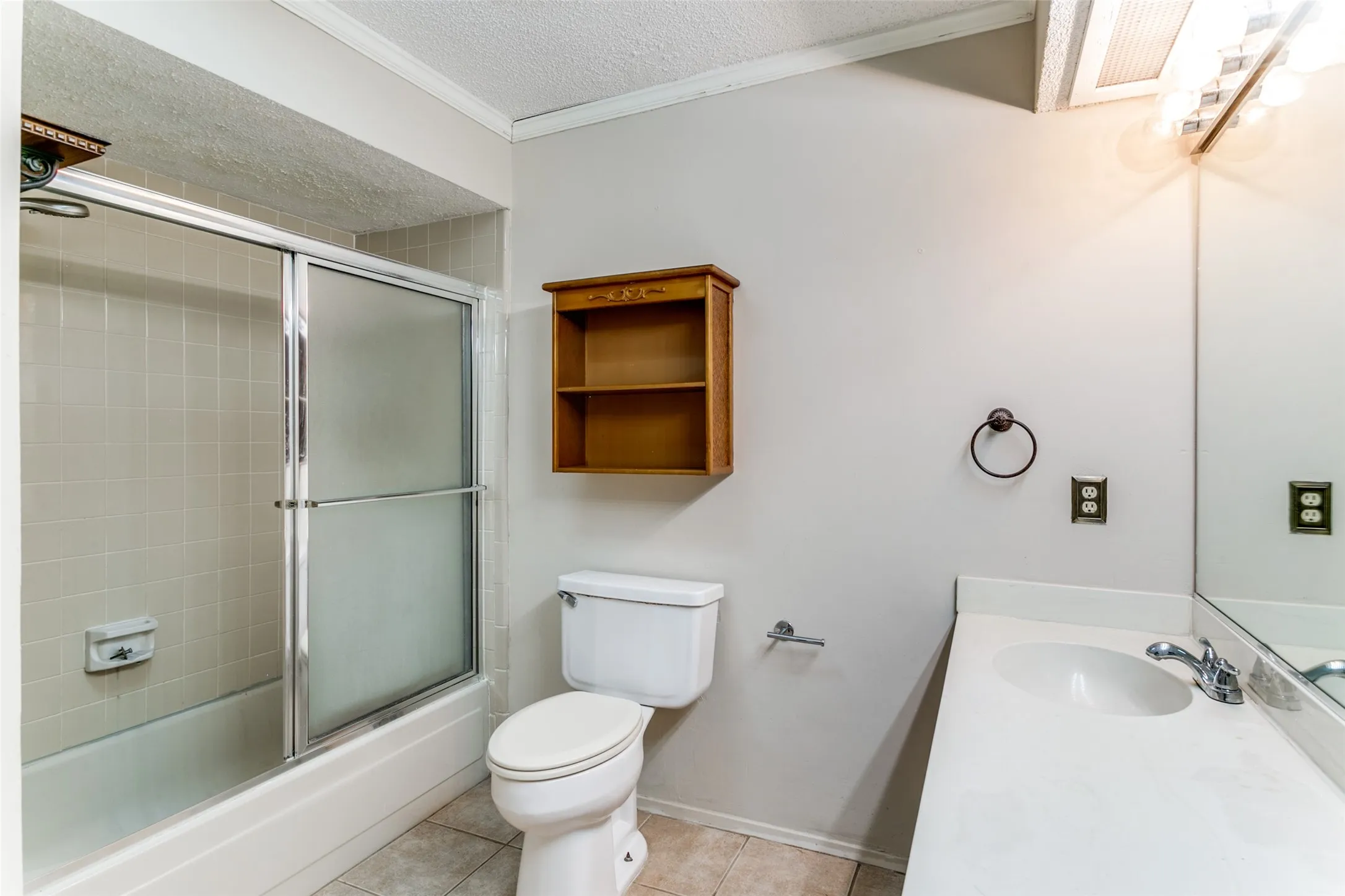 Bathtub with sliding shower doors, single vanity with integrated sink, wall-mounted mirror, and tile flooring