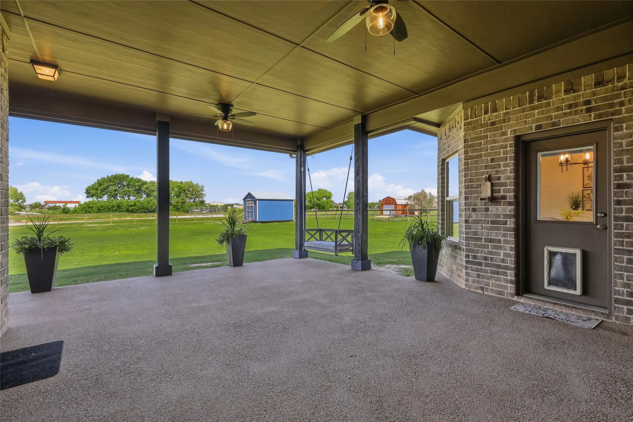 Covered patio featuring an exposed aggregate concrete surface, a brick exterior wall, and ceiling fans
