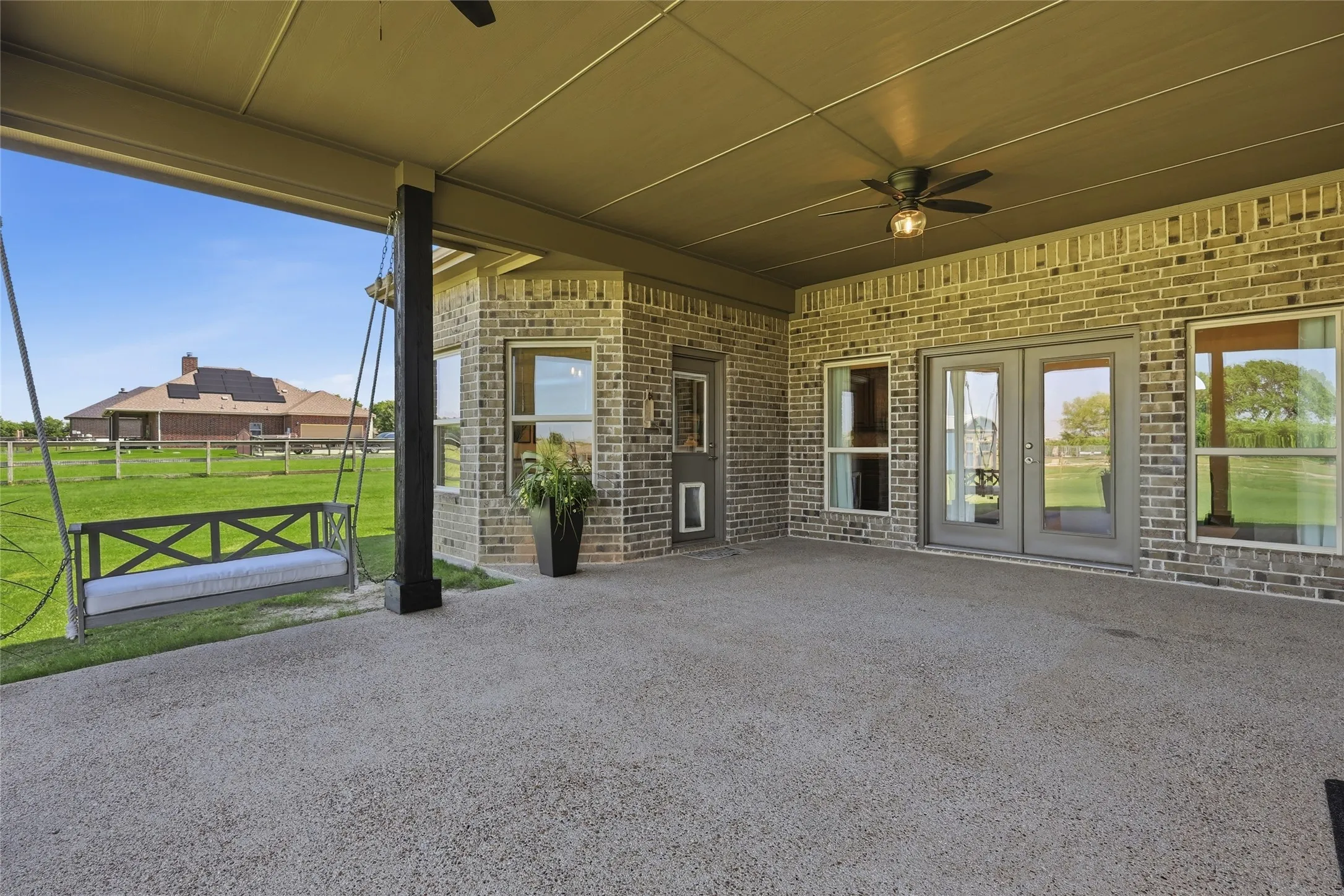 Covered patio with exposed aggregate flooring, brick exterior, ceiling fan, and multiple exterior access points