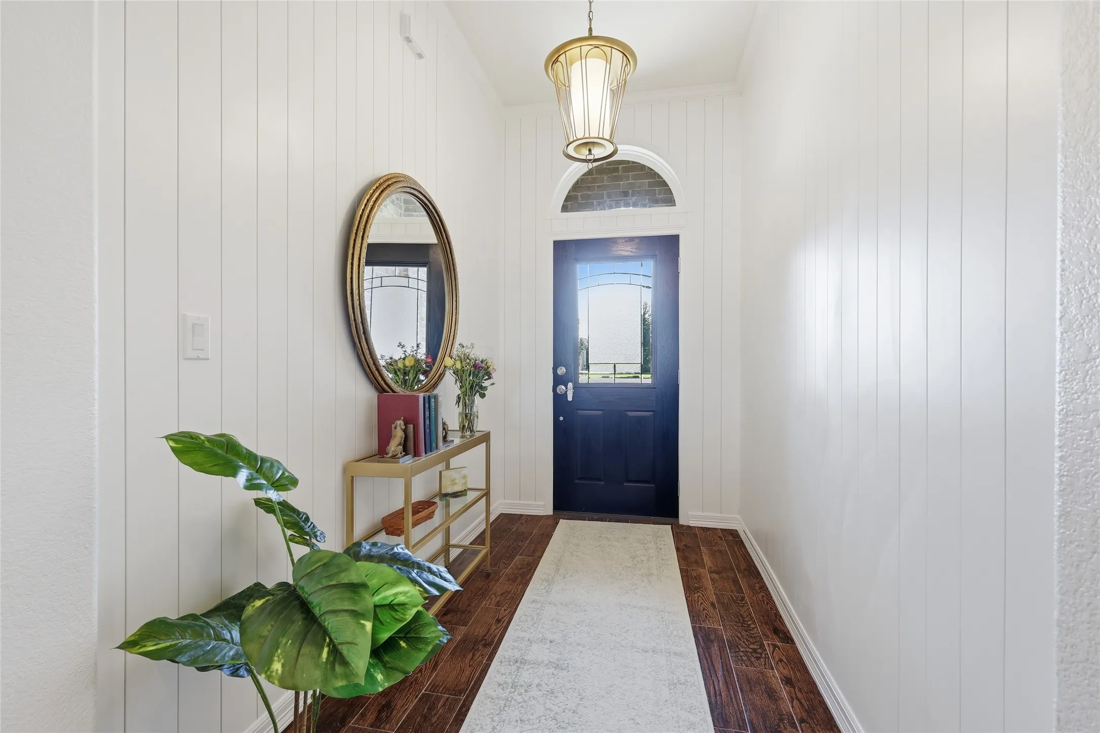 Entryway featuring wood-finish flooring, white vertical paneling, a dark-paneled door with an arched transom, and a decorative pendant light