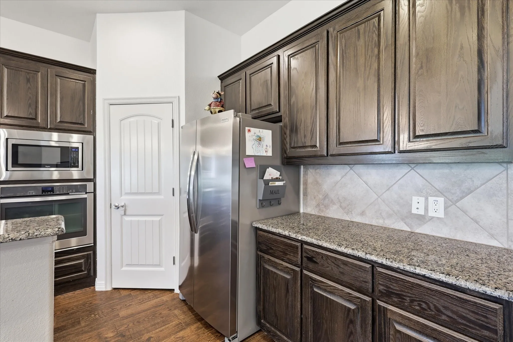 Wood-finish flooring, dark wood cabinetry, stainless steel appliances, granite countertops, and a tiled backsplash