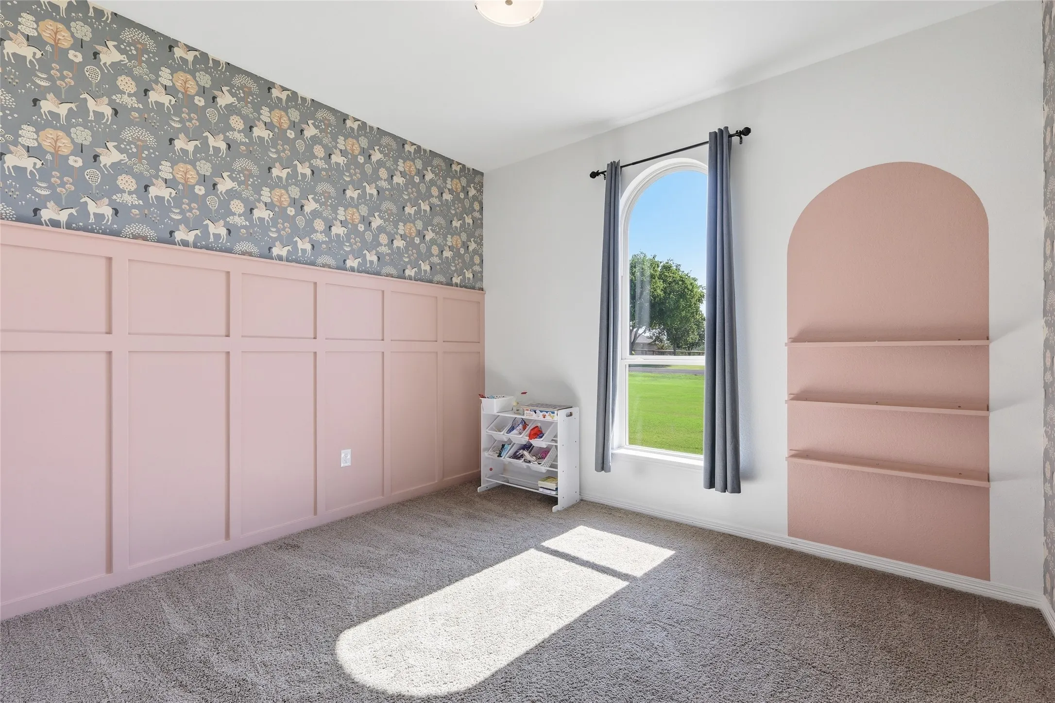 Patterned wallpaper, wainscoting paneling, arched window, built-in shelving, and carpet flooring