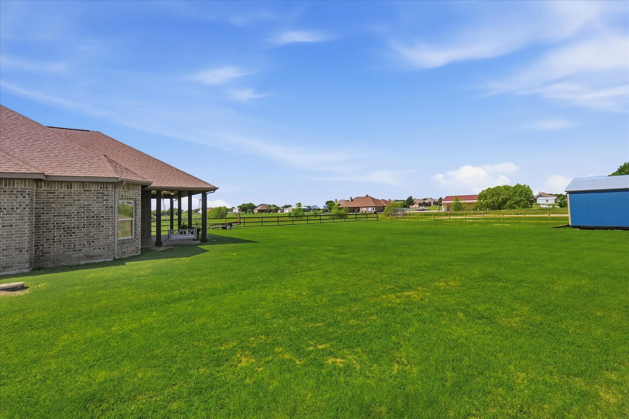 Expansive green lawn with a covered patio, brick exterior, and a blue detached shed