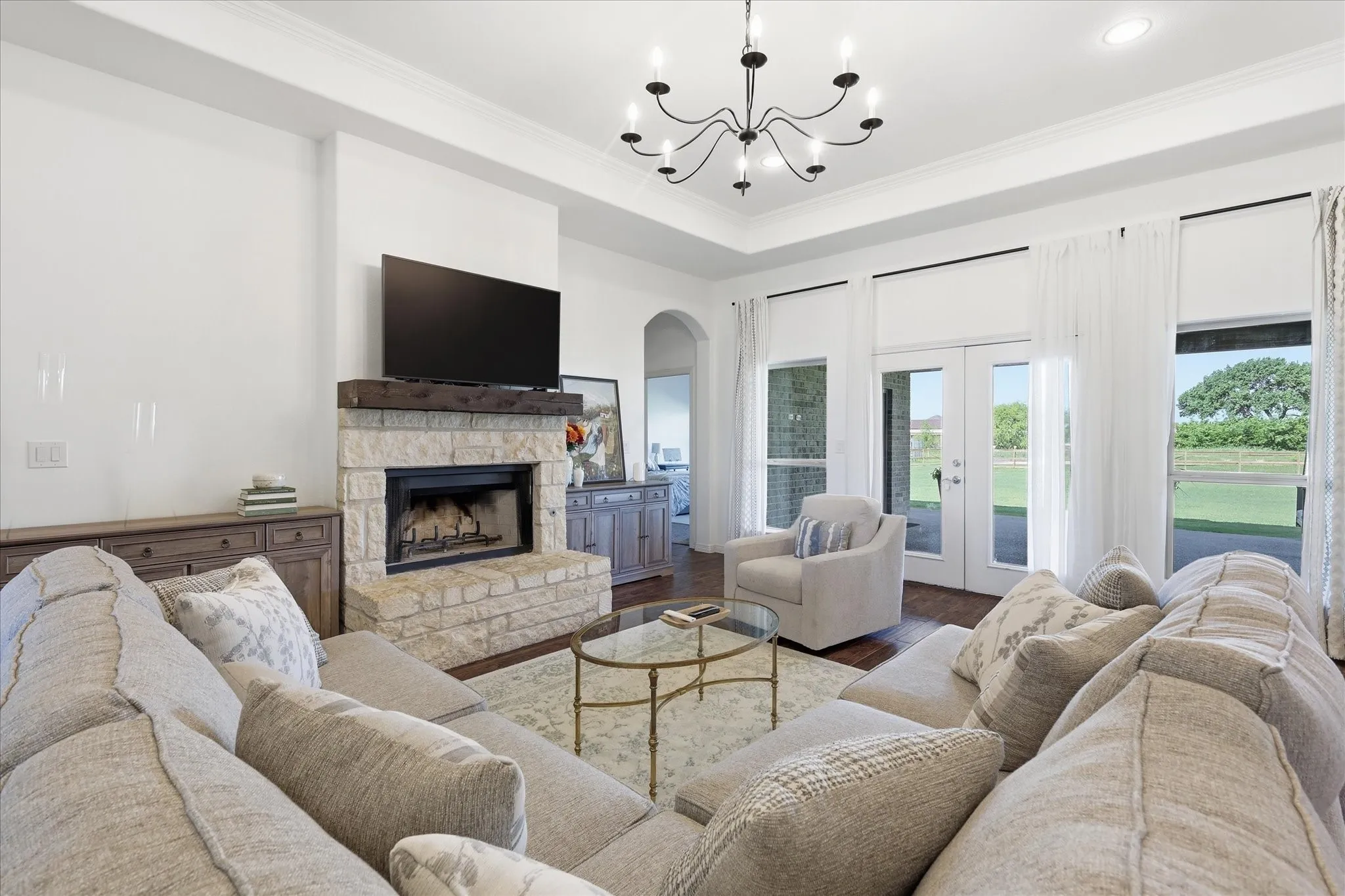 Stone-clad fireplace with a wood mantel, wood-finish flooring, and multiple glass-paned doors