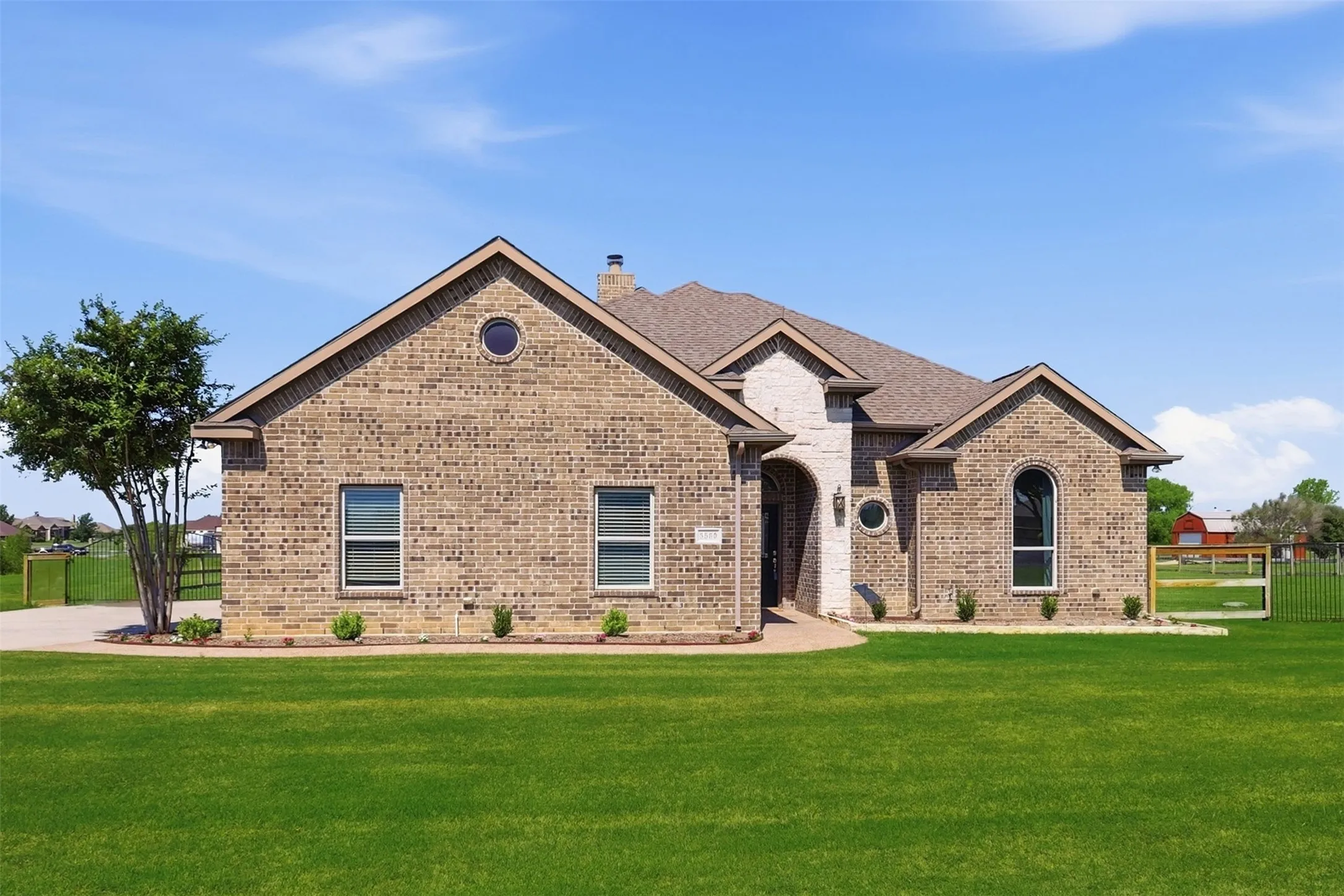 Brick exterior with contrasting stone accents, arched entry, circular window, and established front landscaping