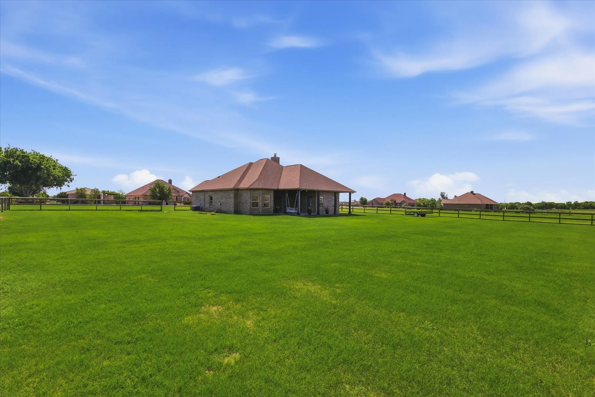 Expansive green lawn with a wood plank fence, a mature tree, and a brick exterior home featuring a covered patio