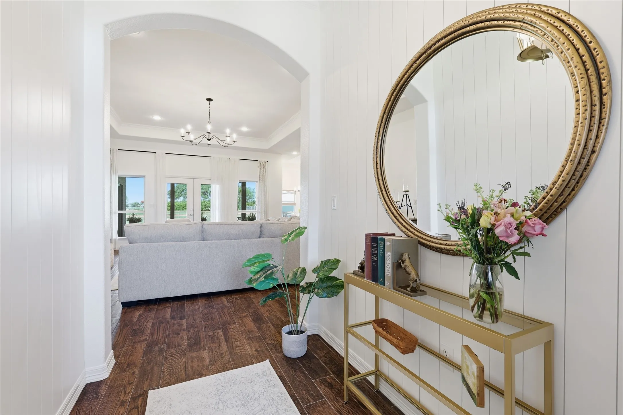 Archway entry with wood-finish flooring, white shiplap wall accent, and an overhead chandelier in the background