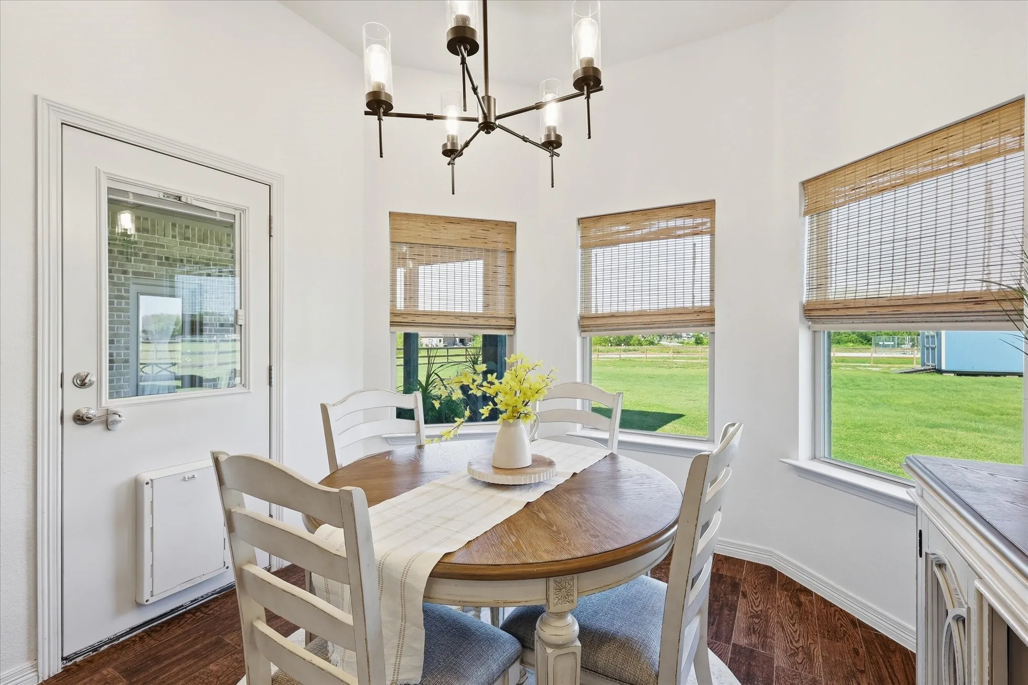 Angled bay windows with woven blinds, modern chandelier, and wood-finish flooring