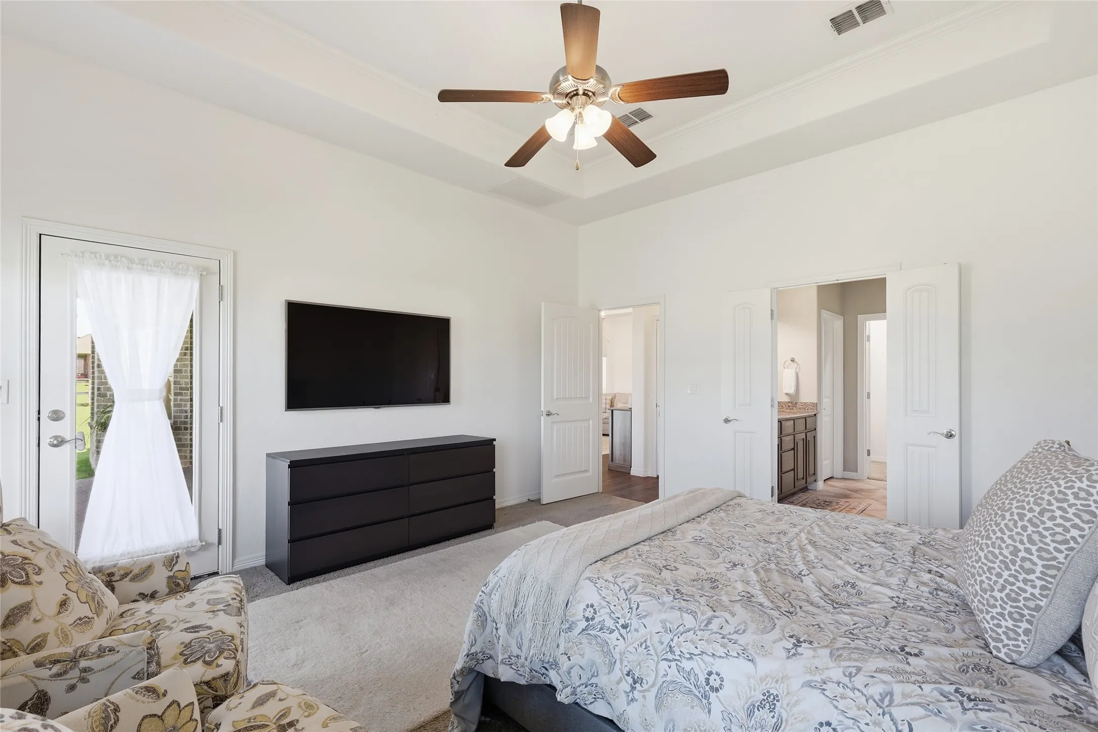 Tray ceiling with a ceiling fan, wall-mounted television, and direct outdoor access