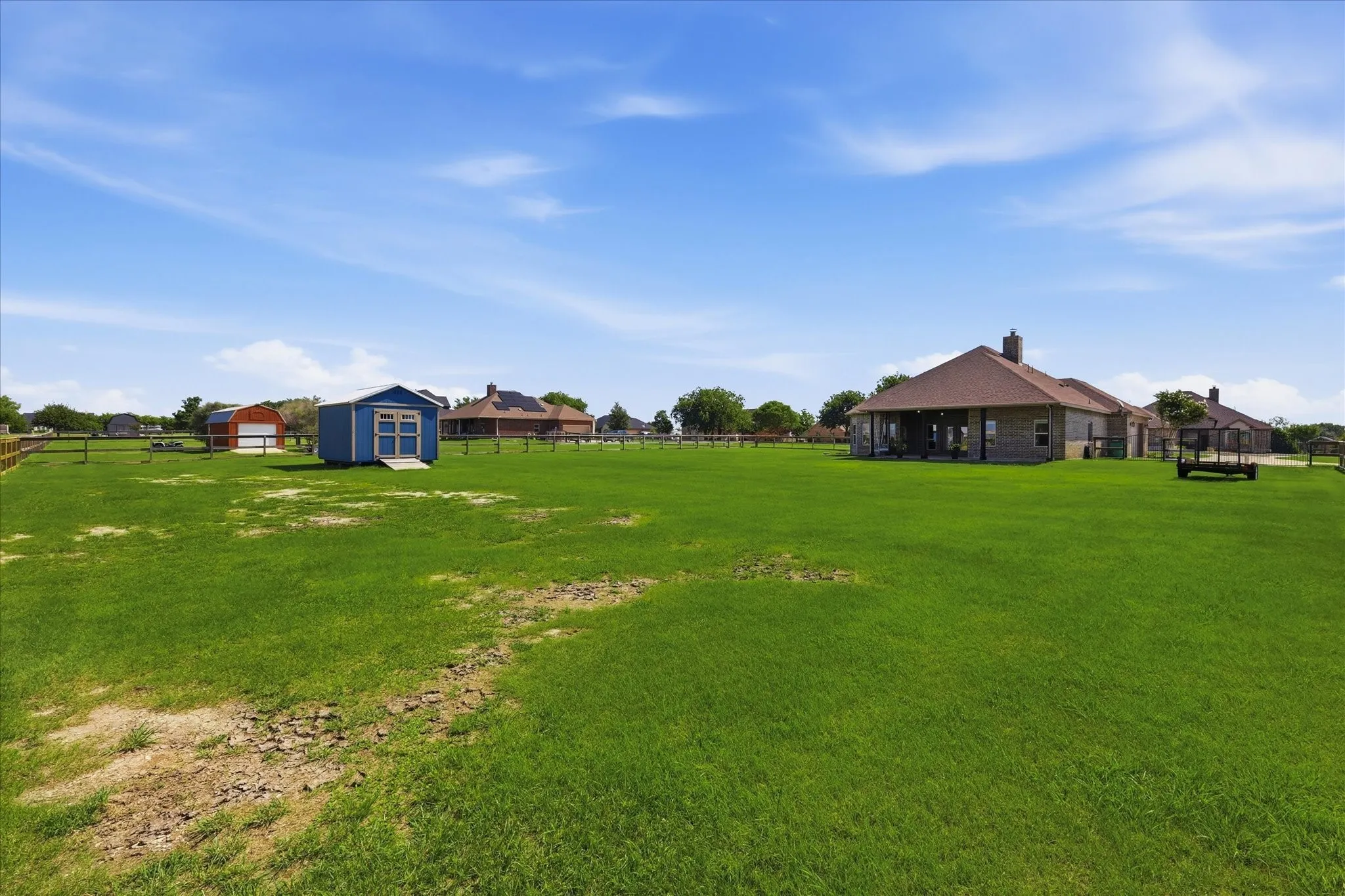 Expansive green lawn with a detached blue shed, a red barn structure, and a covered back patio
