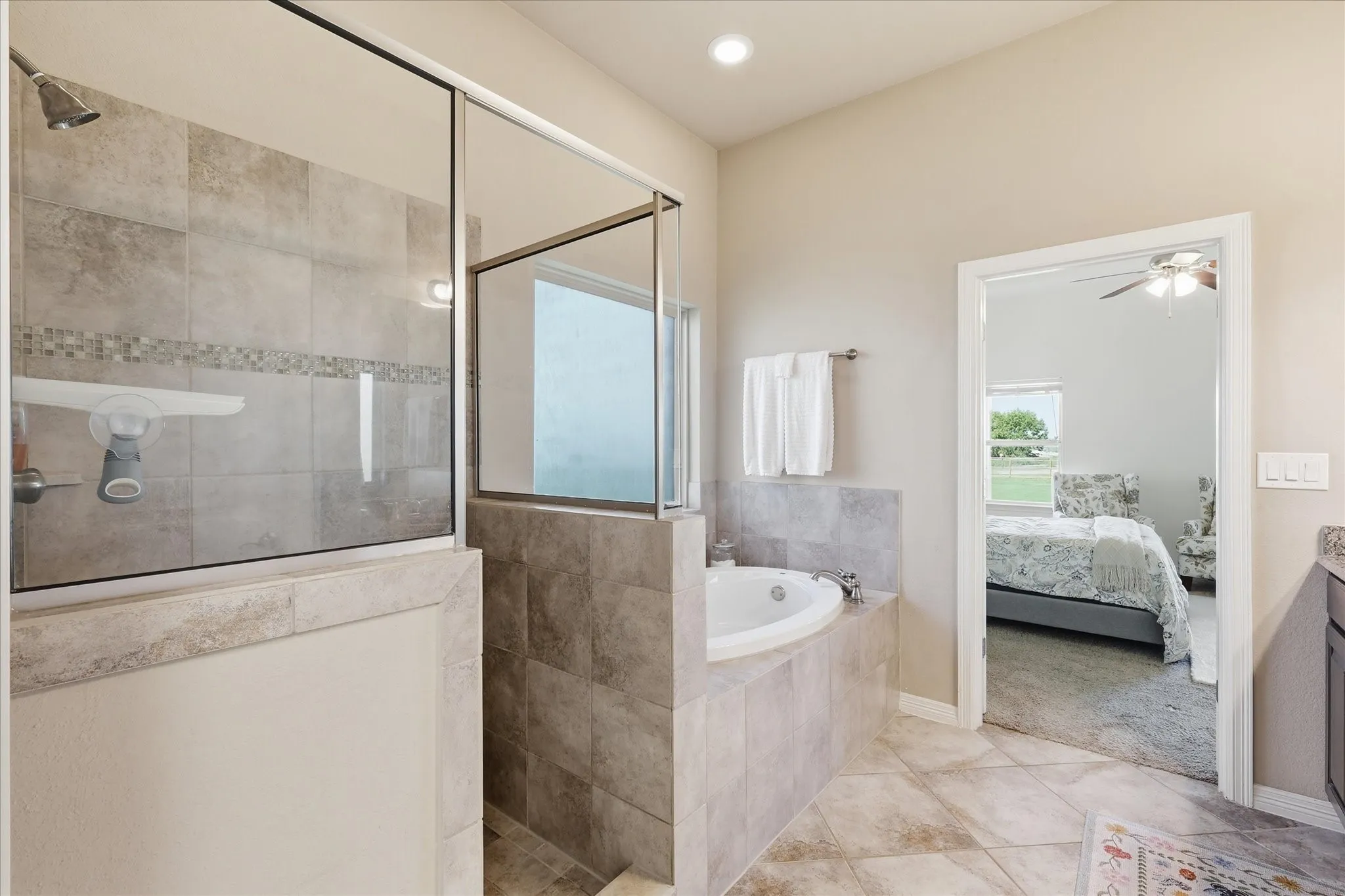 Tiled walk-in shower with a glass enclosure, jetted corner tub, and neutral wall paint