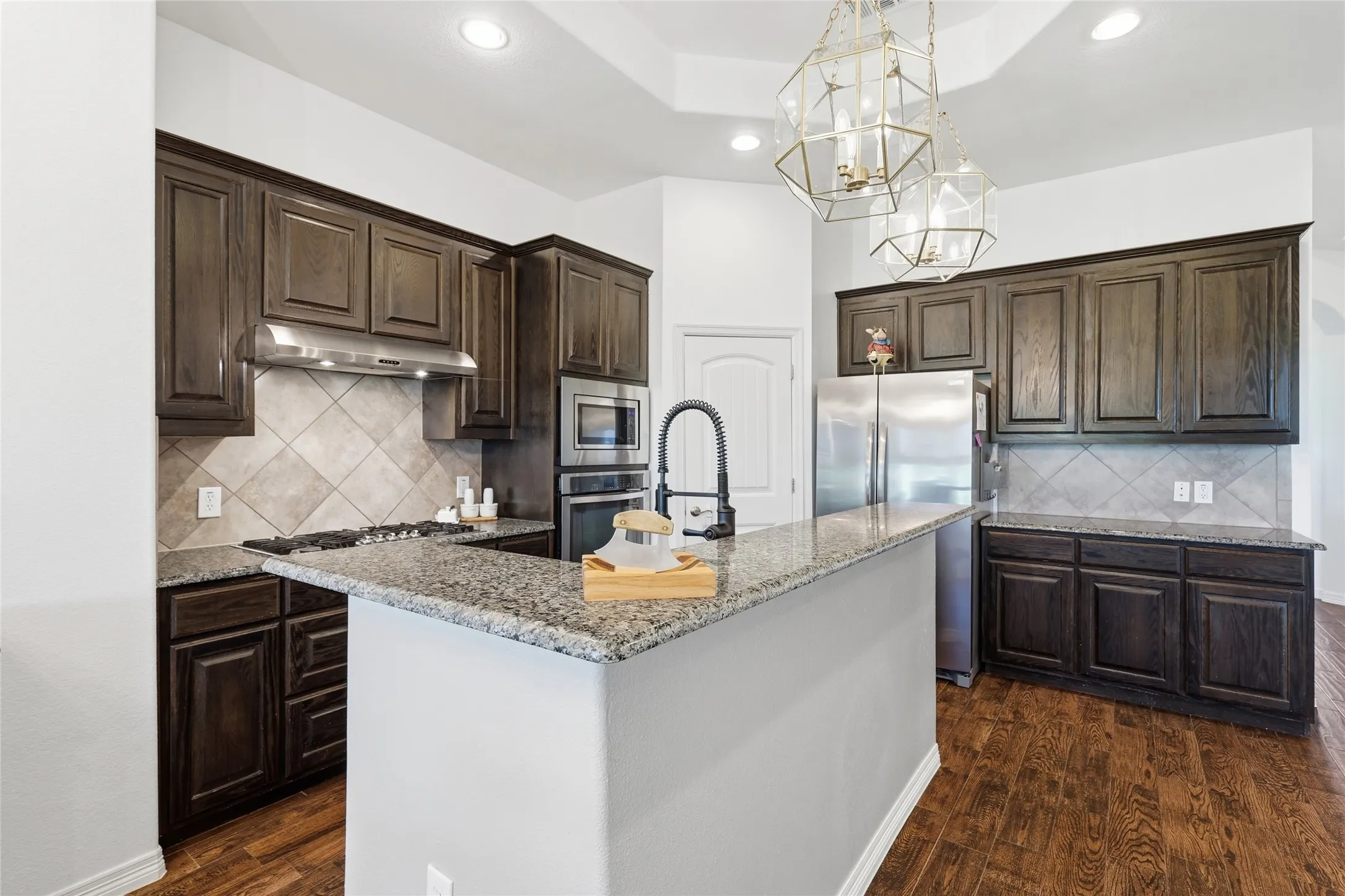Kitchen featuring wood-finish flooring, dark wood cabinetry, light-toned granite countertops, and stainless steel appliances