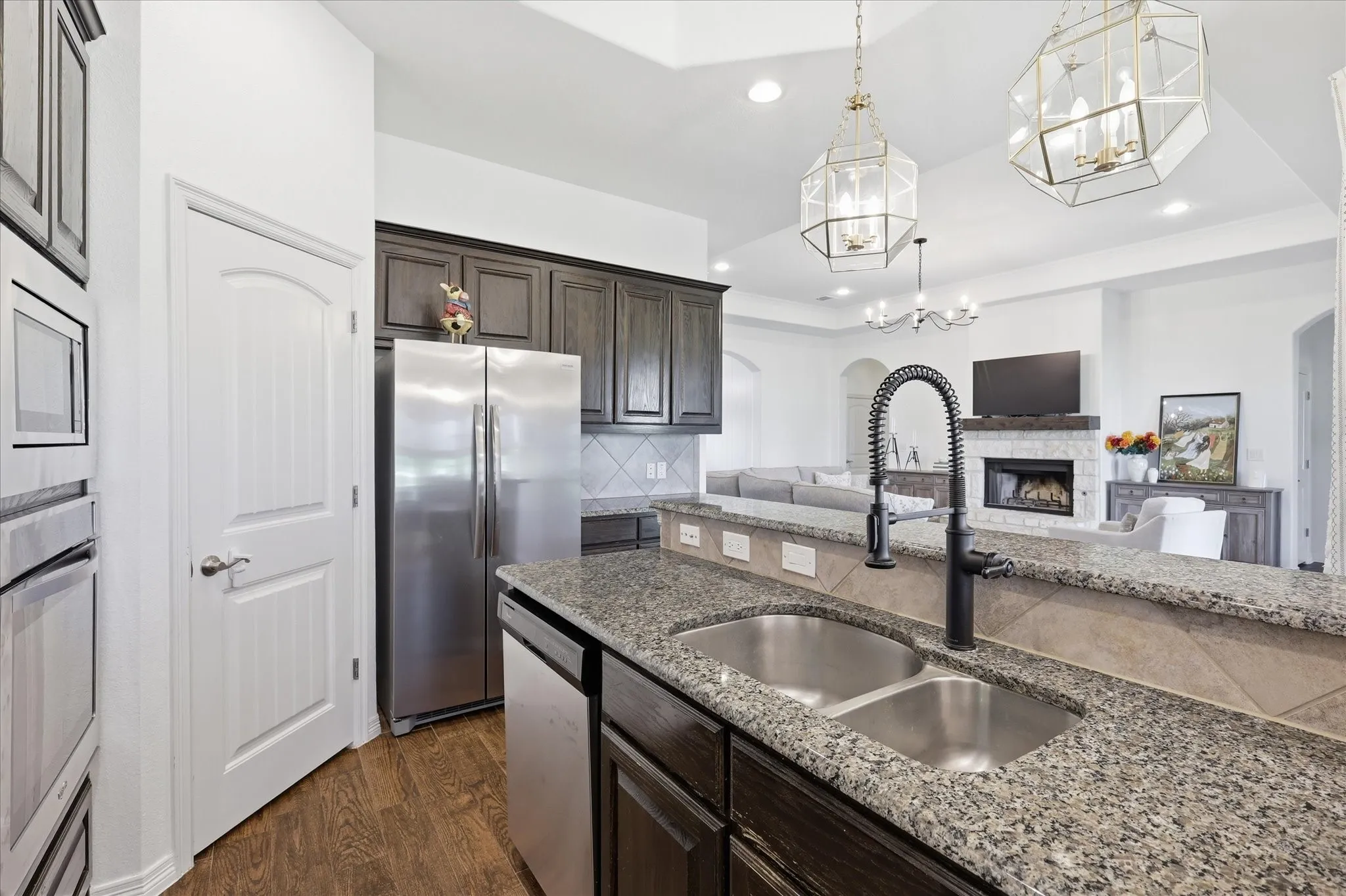 Kitchen featuring dark wood-finish cabinetry, stainless steel appliances, speckled stone countertops, and a double basin sink with a matte black faucet