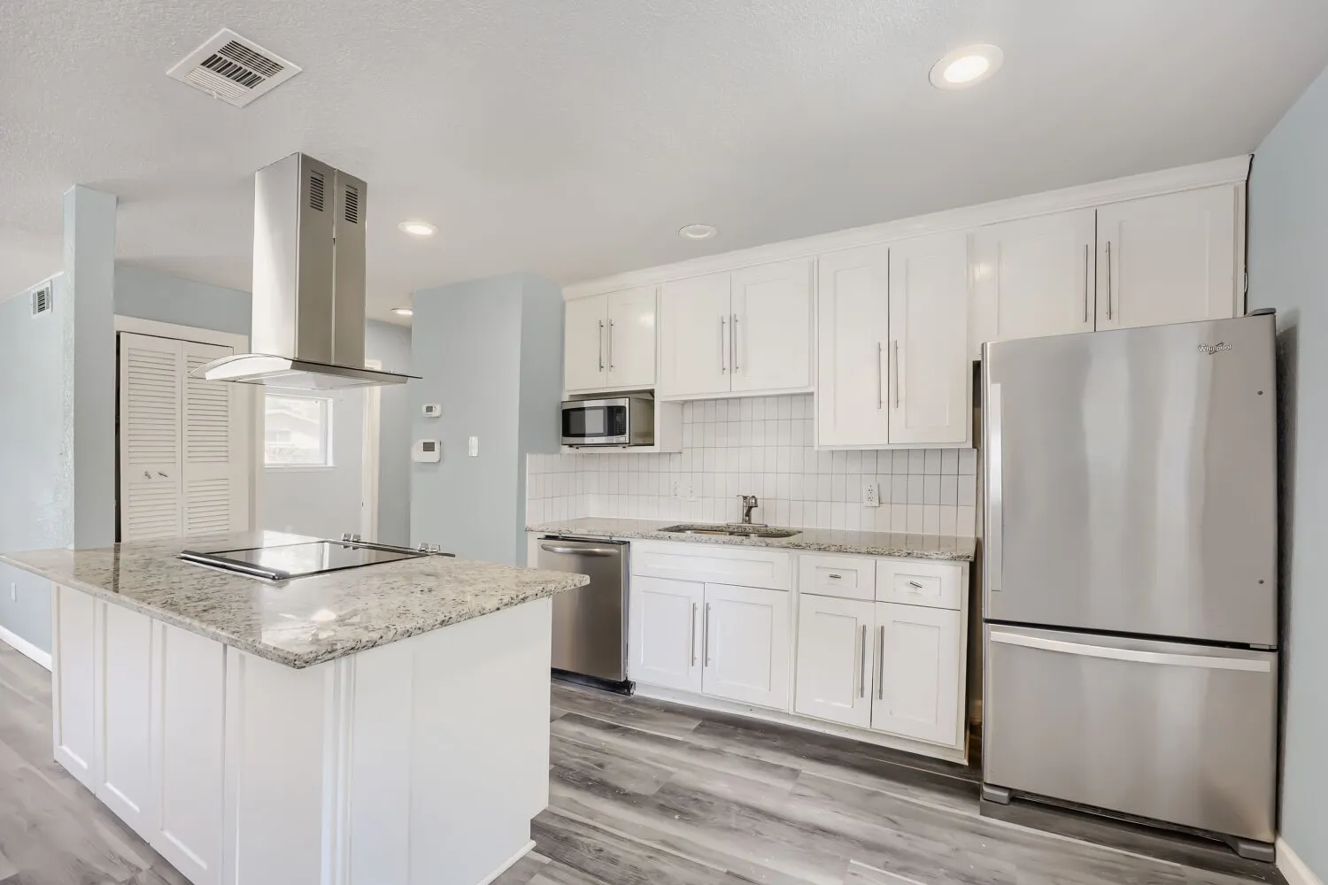 Kitchen featuring an island with a built-in cooktop, stainless steel range hood, white cabinetry, granite countertops, and stainless steel appliances