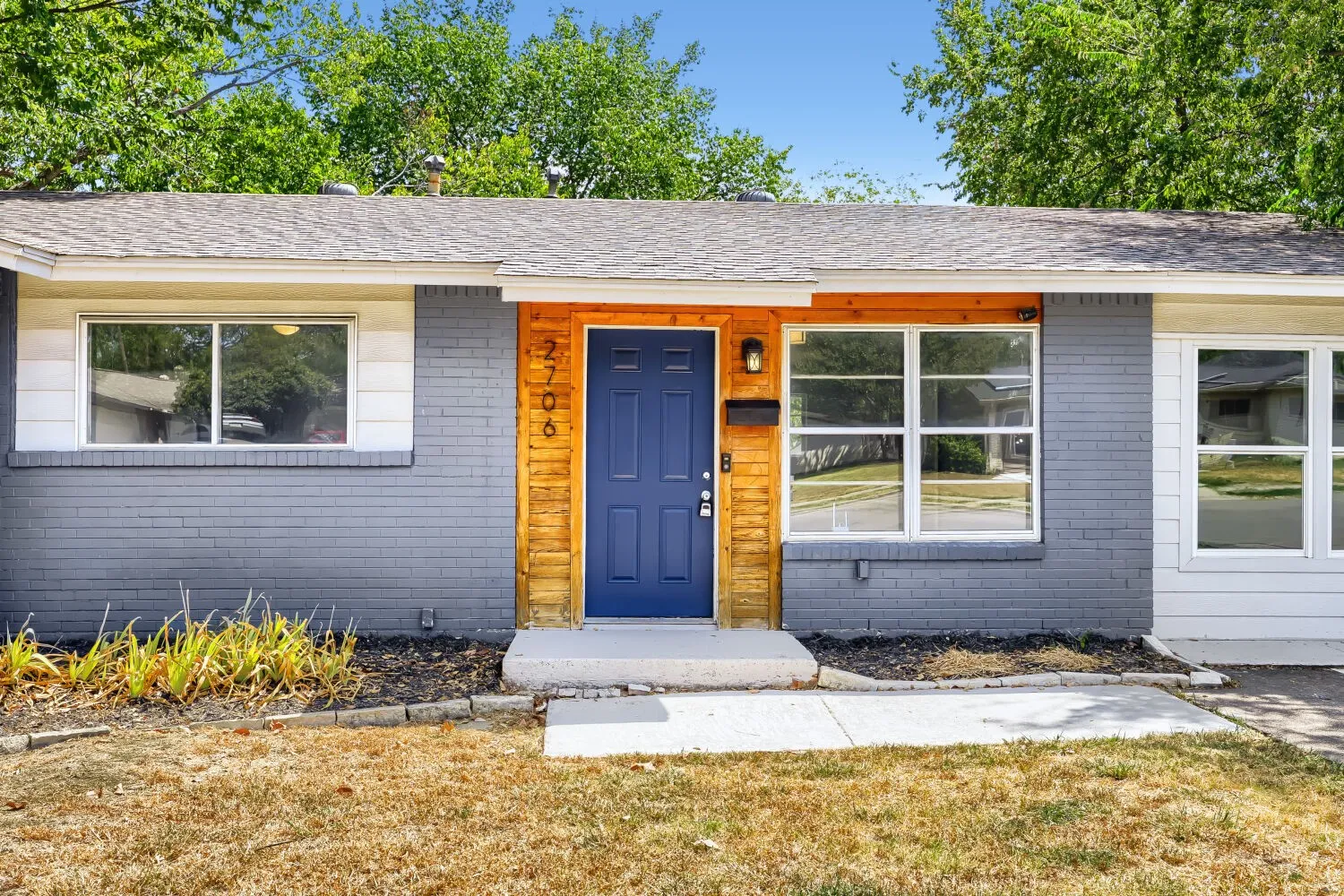 Exterior featuring gray brick and white siding, wood-paneled entry, blue paneled door, and a shingle roof