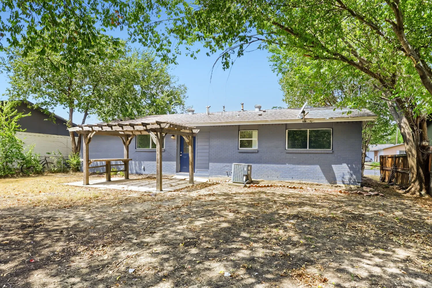 Backyard featuring a wood pergola over a concrete patio, a blue painted exterior, and mature trees