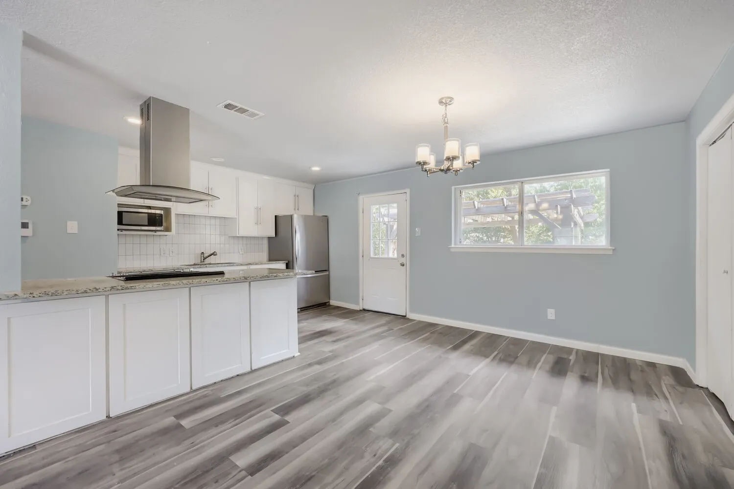 Open-concept kitchen and dining area featuring wood-finish flooring, white cabinetry, stainless steel appliances, and a tiled backsplash