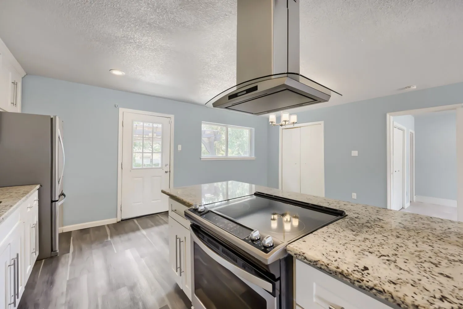 Kitchen featuring an island with built-in cooktop, stainless steel range hood, white cabinetry, and light-toned countertops