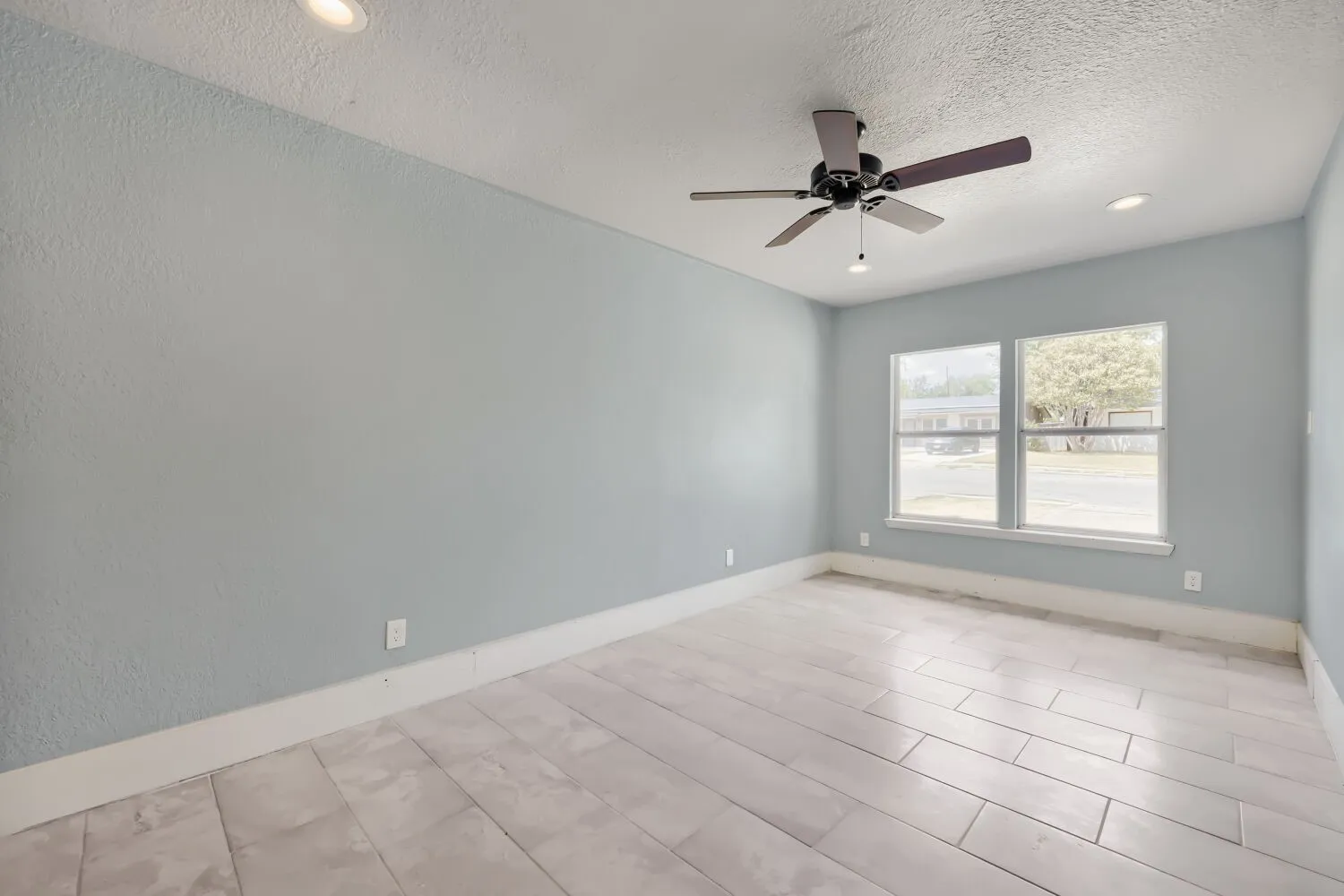 Recessed ceiling lighting, ceiling fan with integrated light, two windows, and wide plank tile flooring