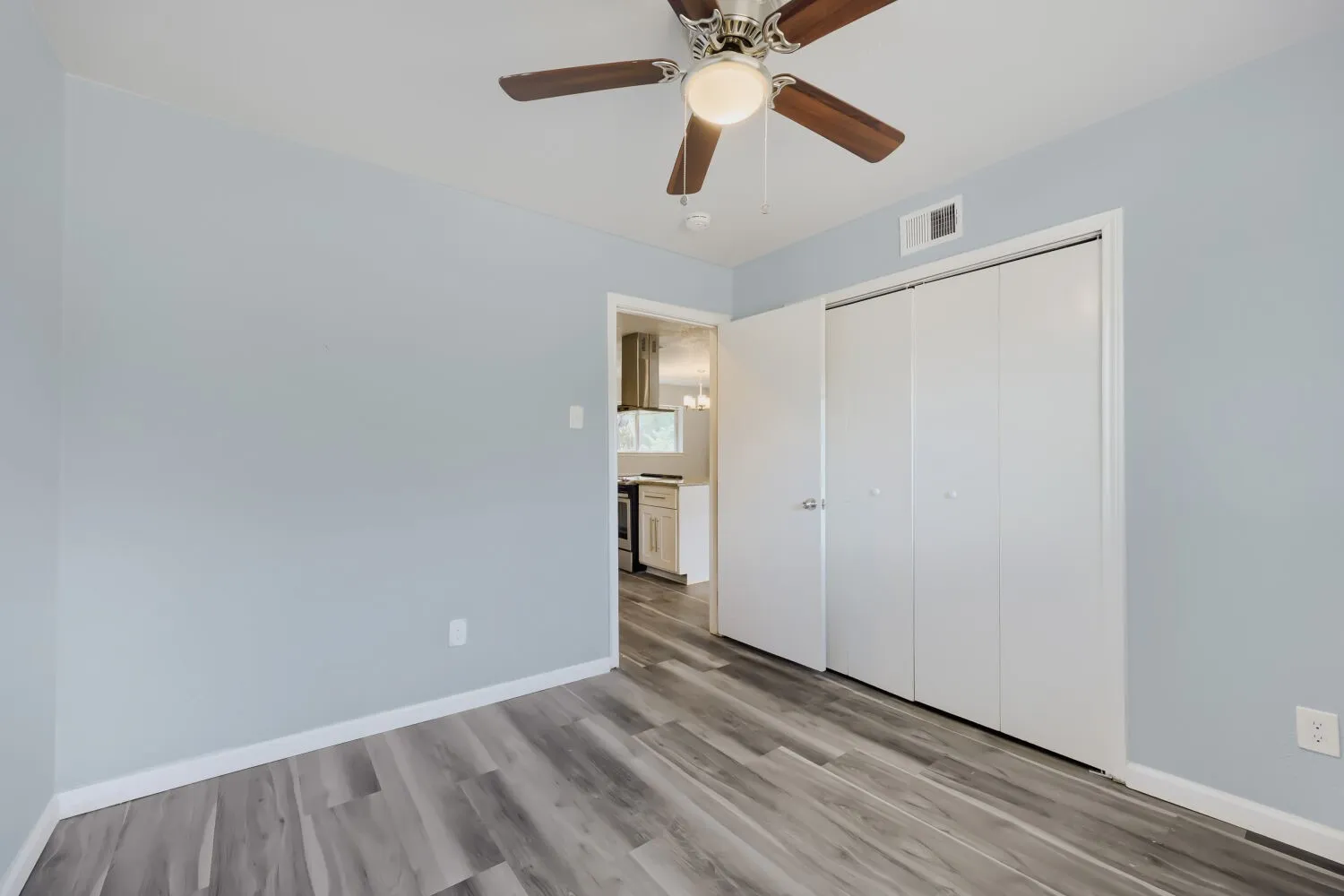 Wood-finish flooring throughout, light blue walls, and a ceiling fan with integrated lighting